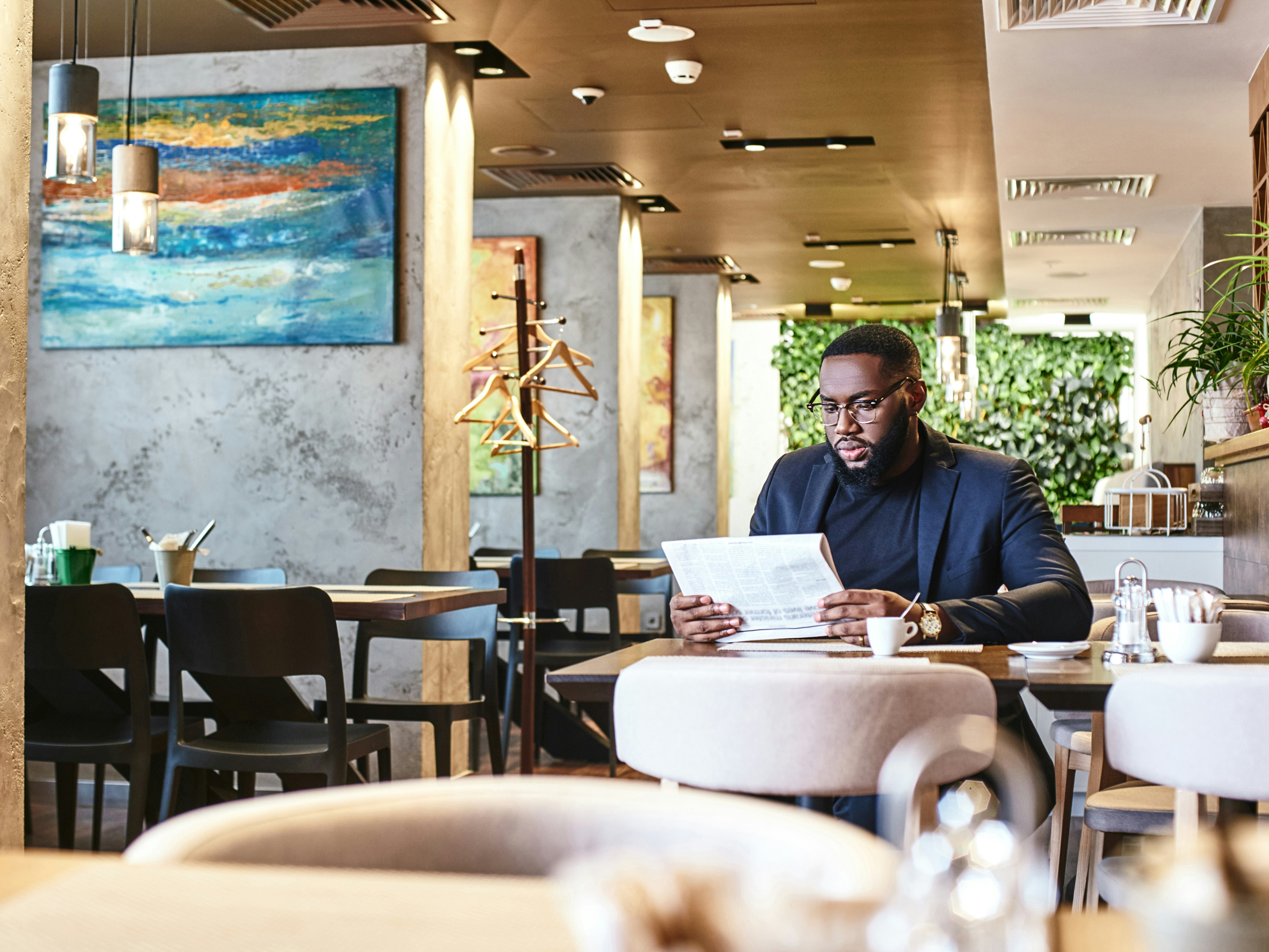 A photo of a person reading a newspaper while sitting at a table in a restaurant