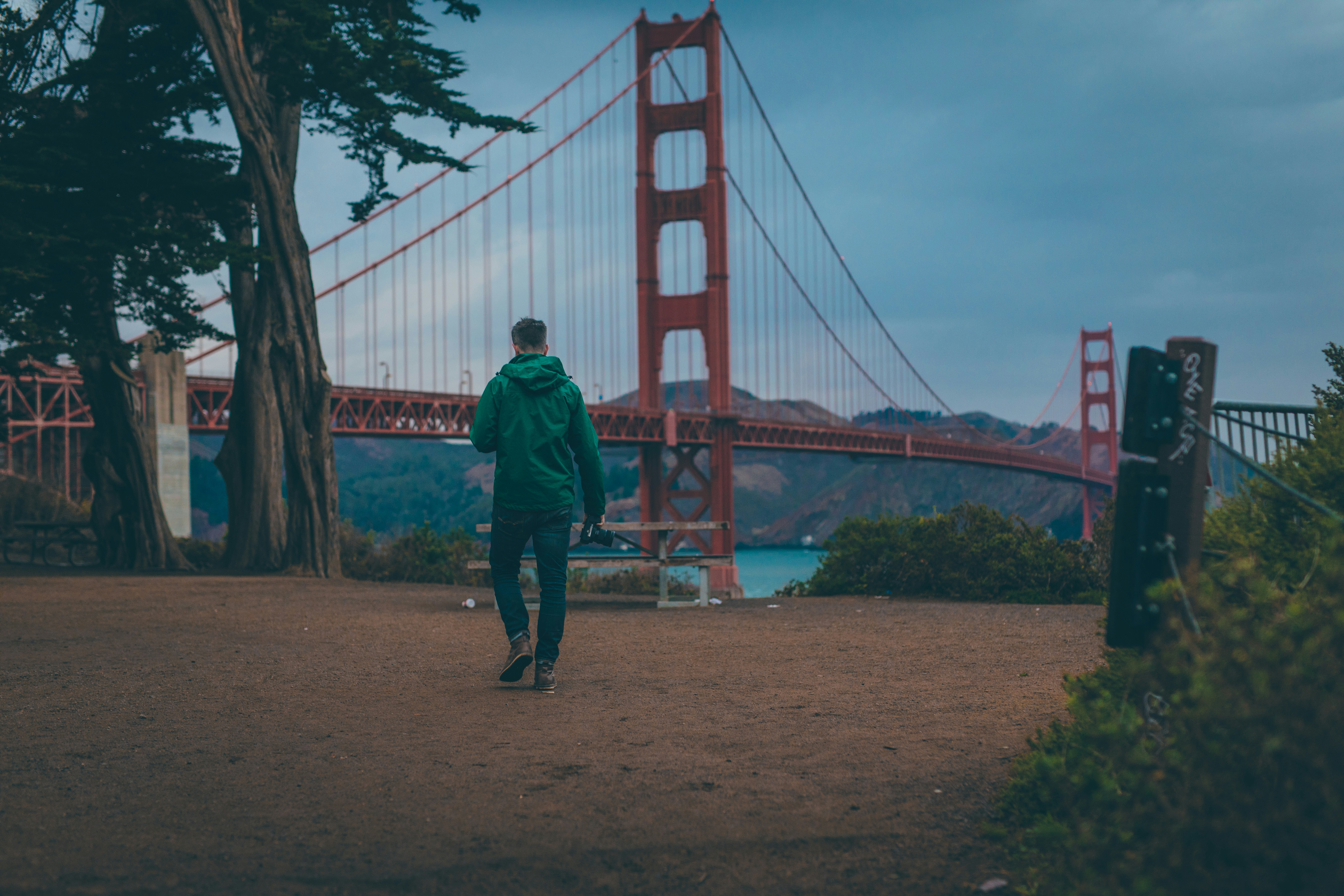 A dirt pathway next to a view of a large, red bridge