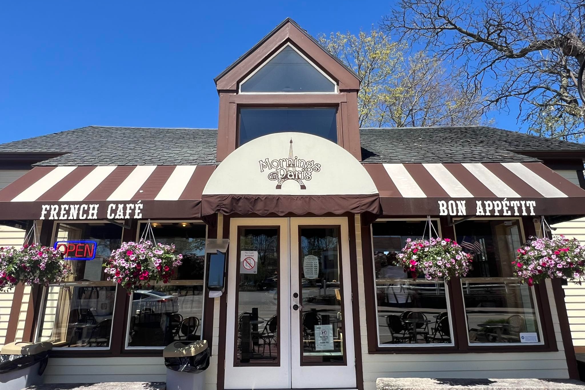 The outside of a French cafe with a brown and white awning