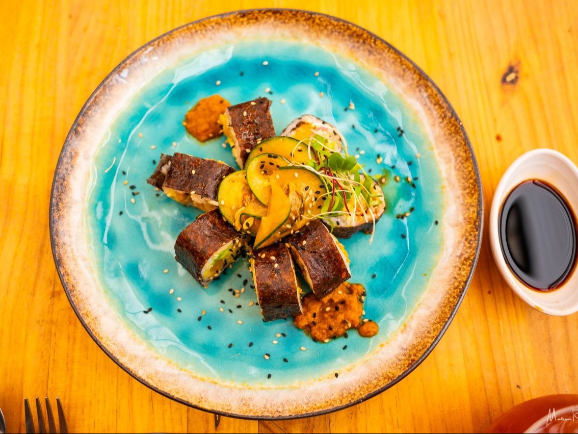 A plate of sliced meat garnished with herbs and avocado and a sauce on a wooden table.