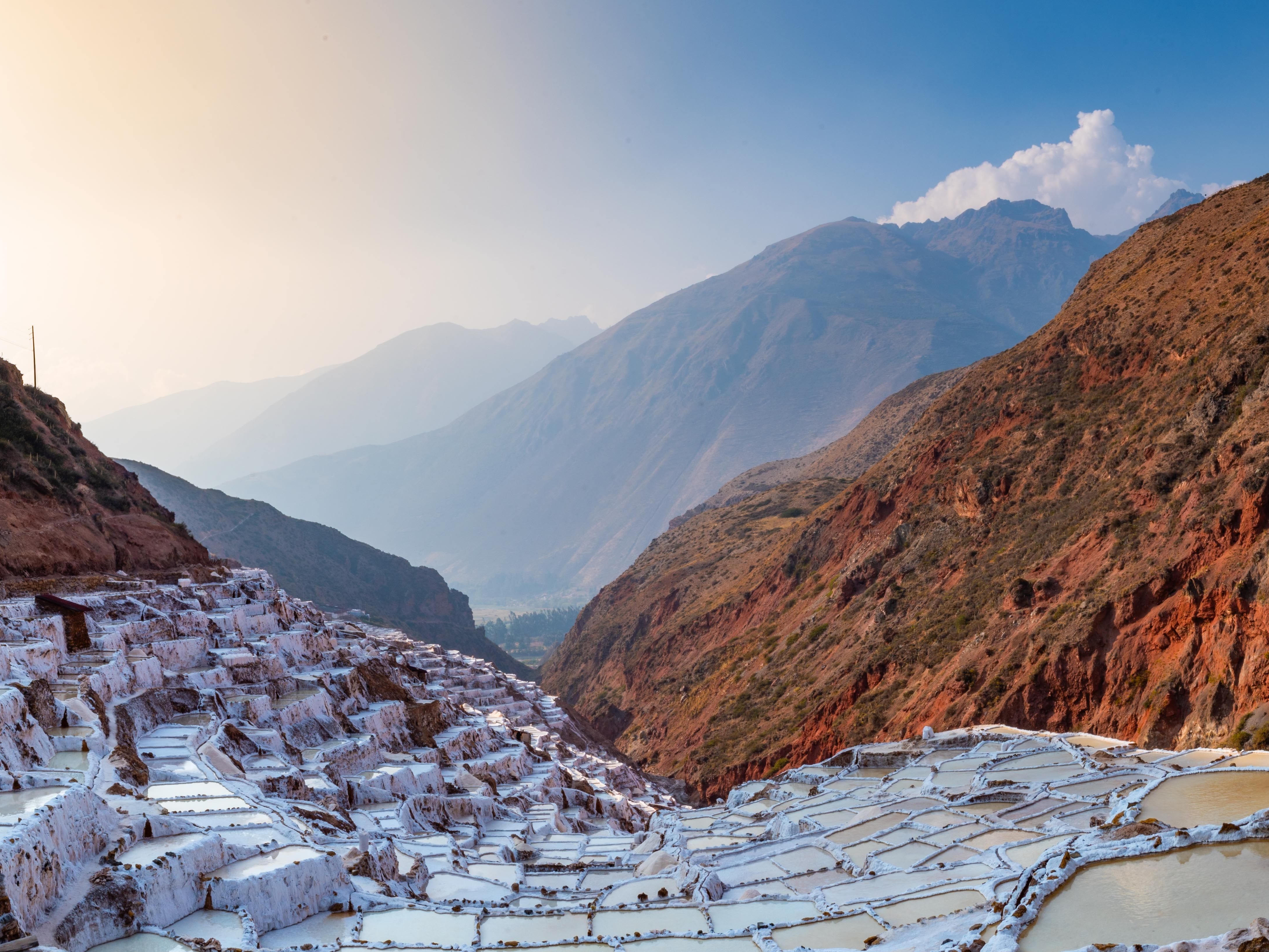 A series of terraced salt evaporation ponds in a mountainous landscape under a clear sky.