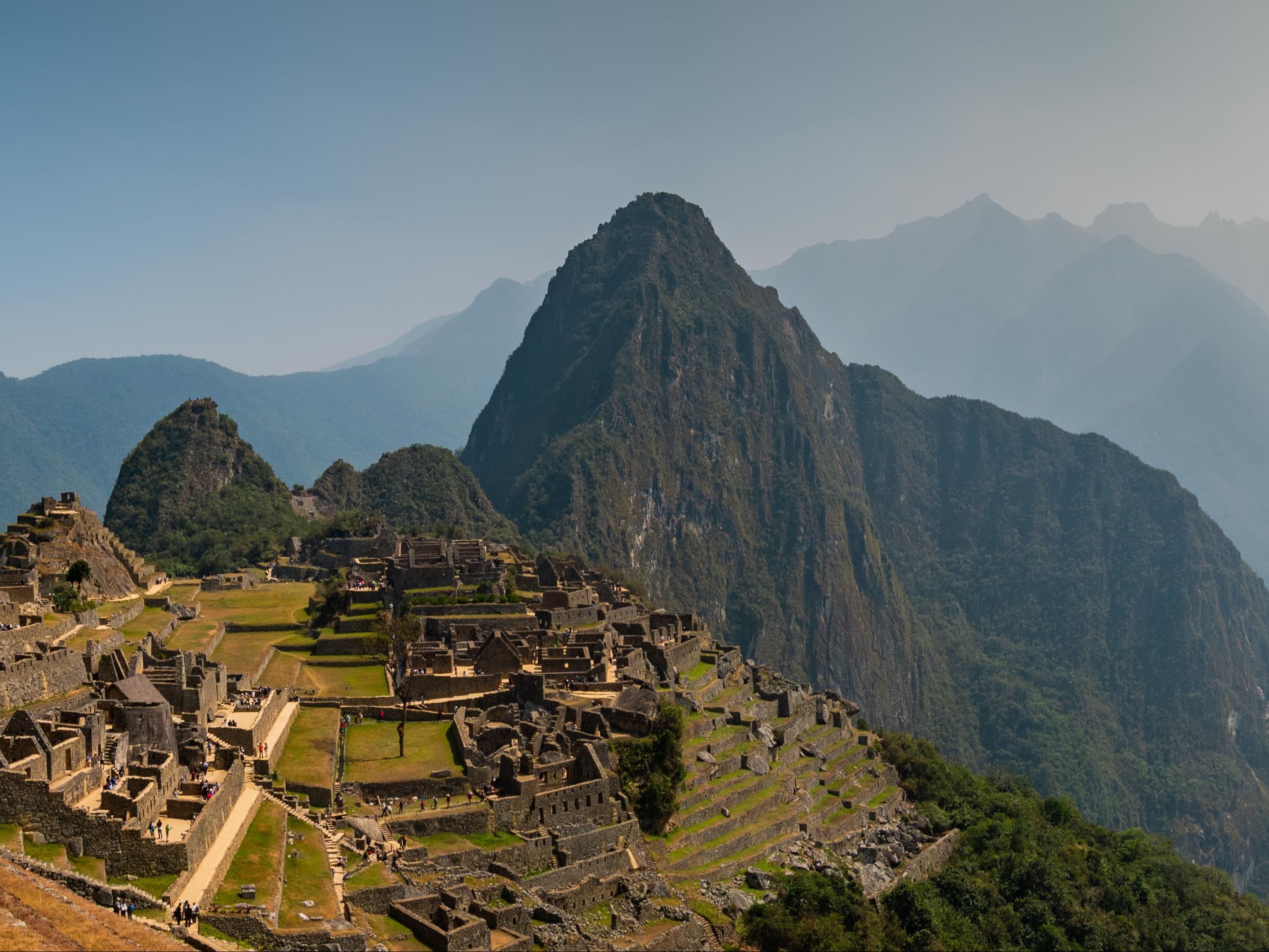 A panoramic view of Machu Picchu with a stunning mountainous backdrop under a clear sky.