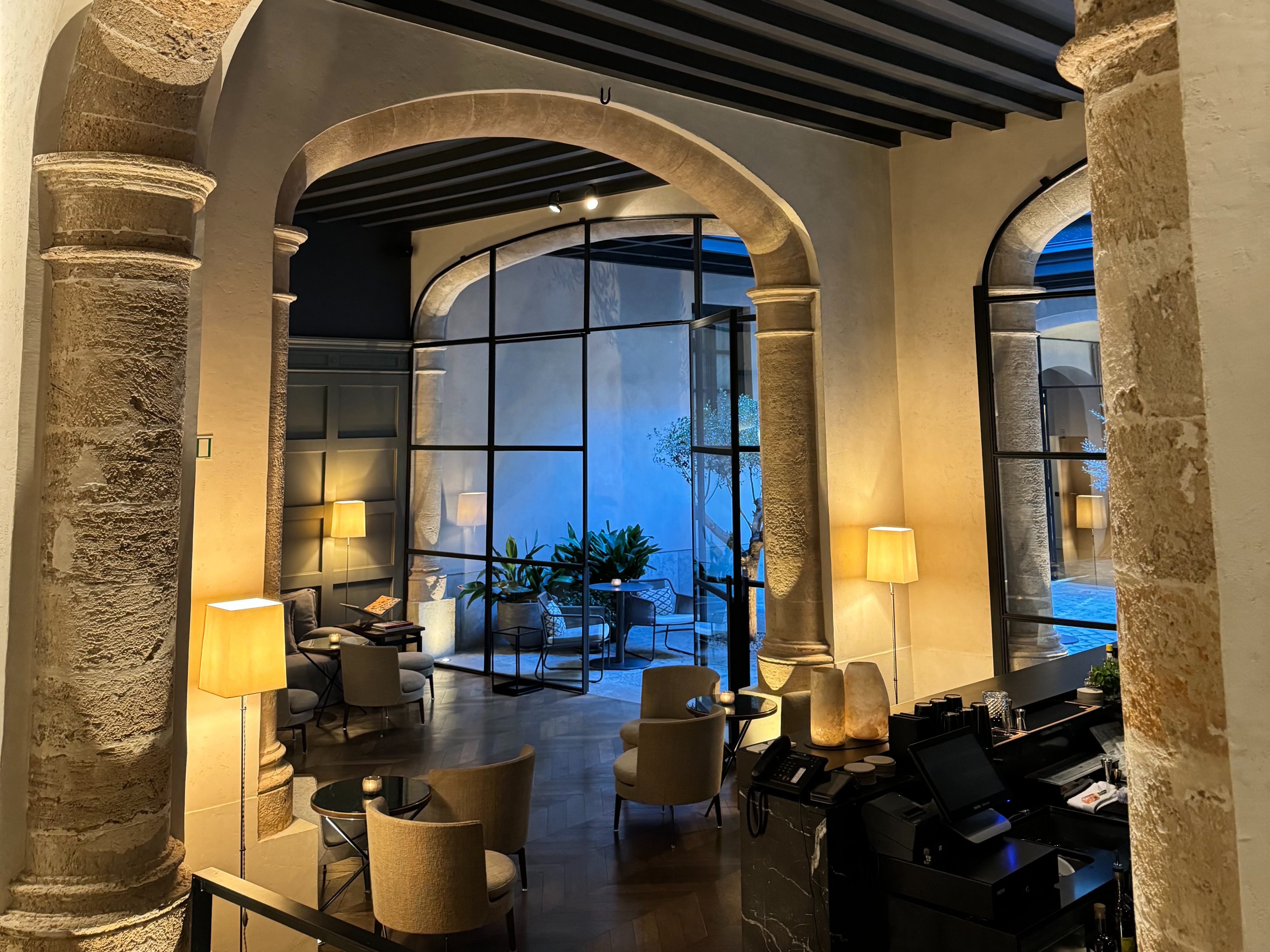 A curved stone archway leads to a cozy room with tables and chairs, viewed from above.