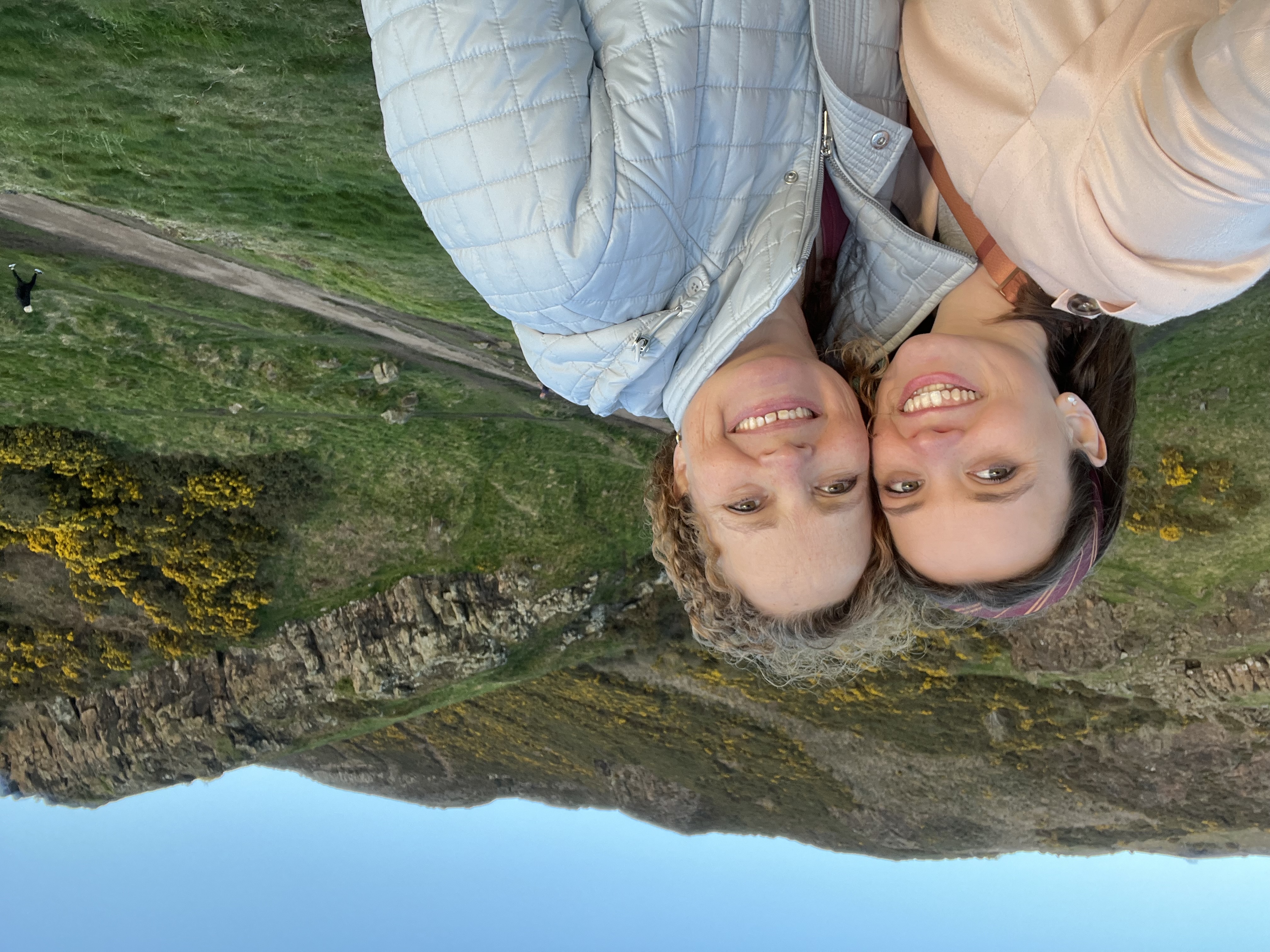 Two women posing in front of a fertile hillside on a clear, windy day.
