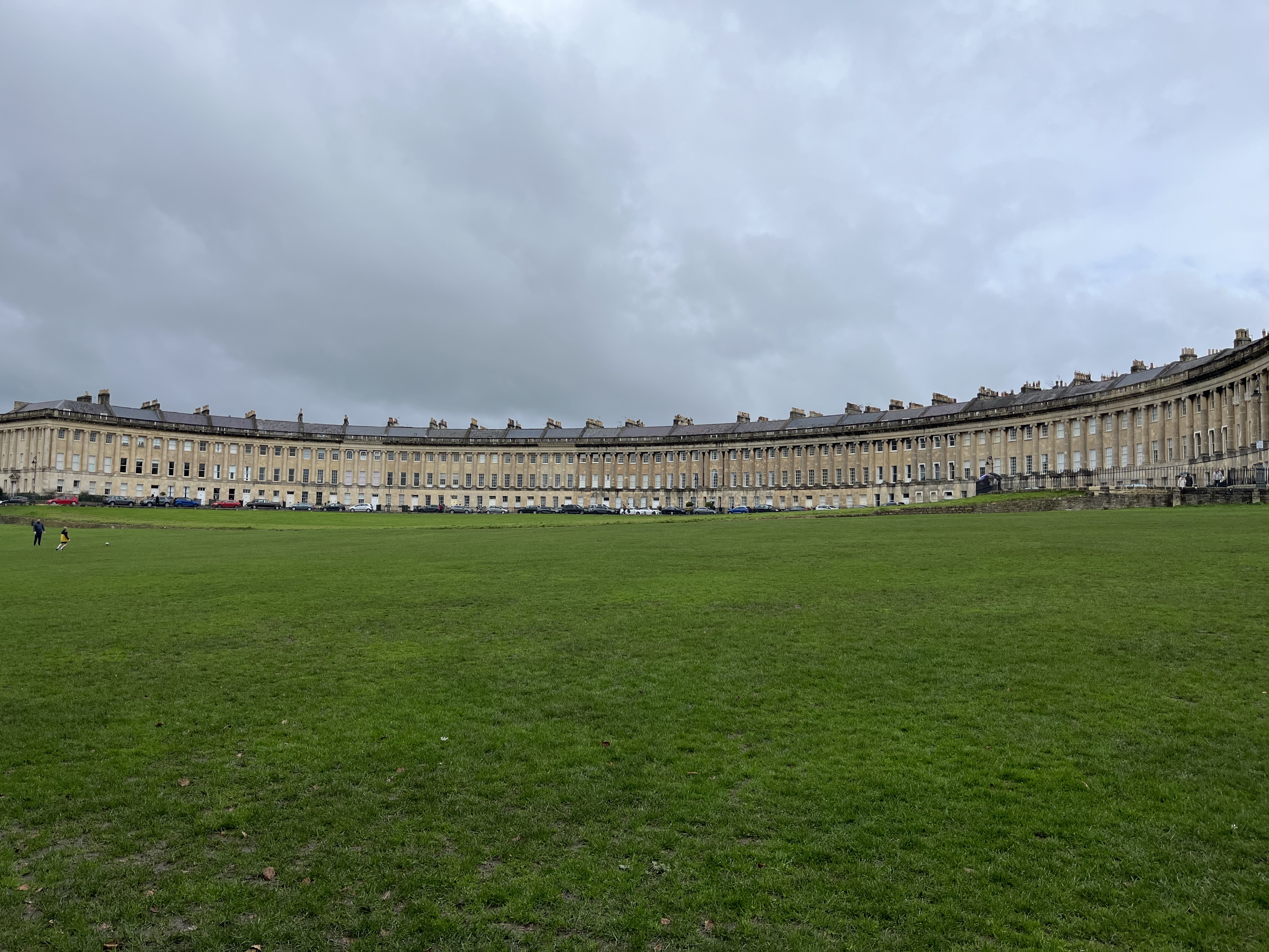 The grassy field expands in front of a crescent-shaped estate on a cloudy day.