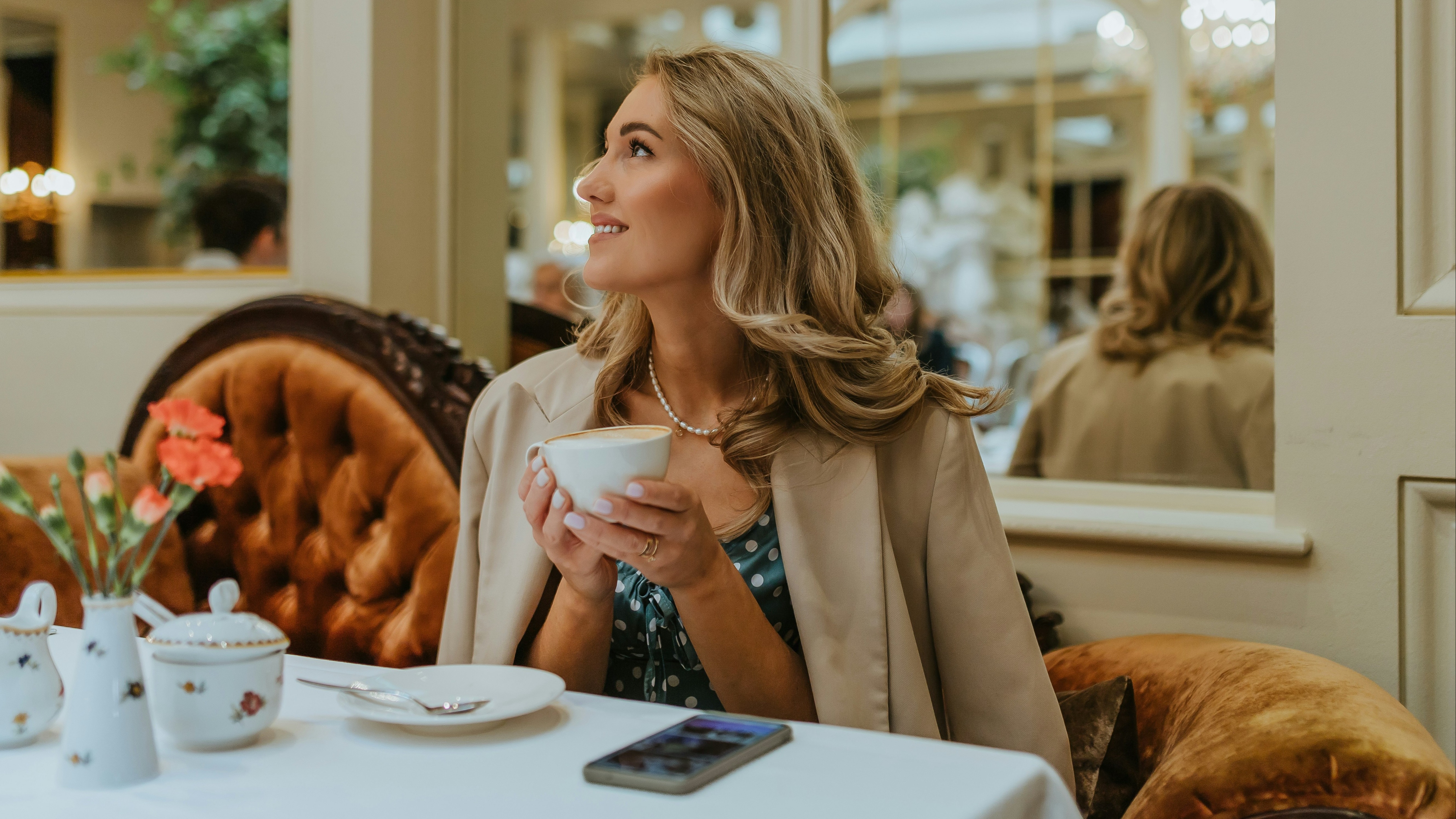 An individual sits at a table in an elegant setting, holding a cup.