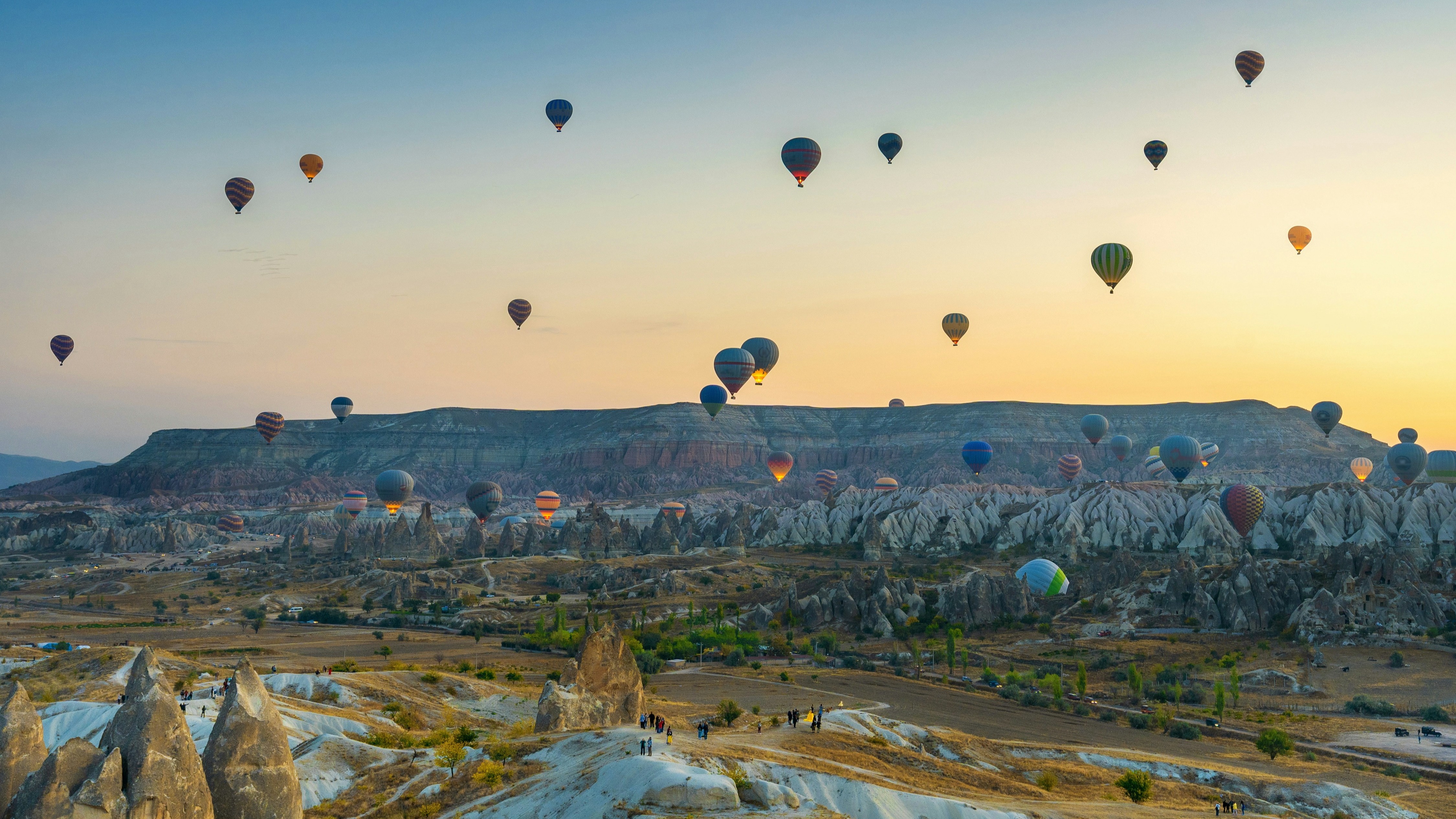 Hot air balloons float gracefully over a rocky landscape at sunrise.