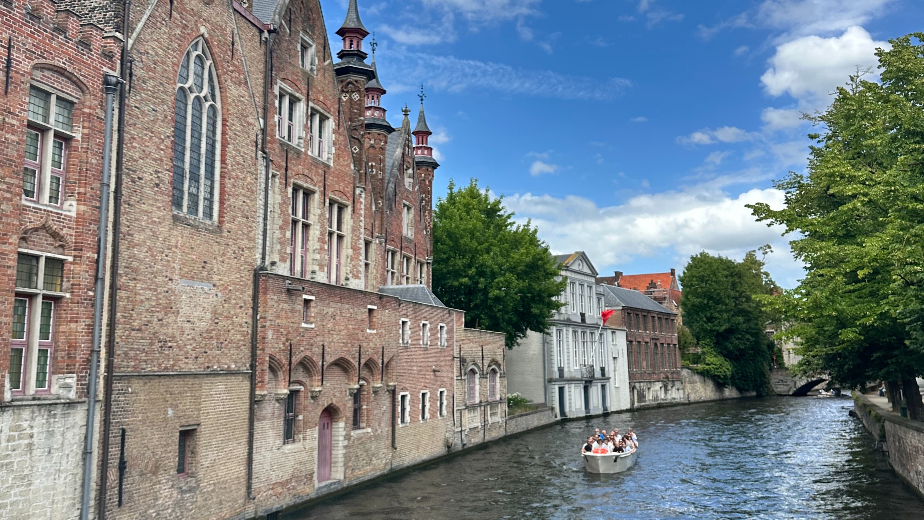 A historic building stands gracefully by the water under clear skies, with a boat floating nearby on a canal.