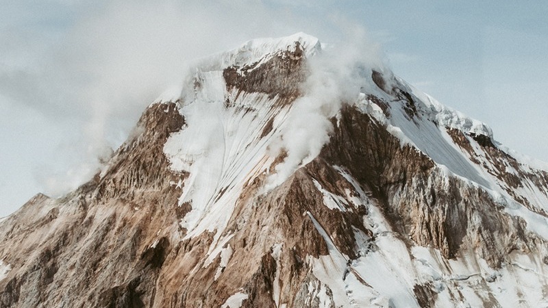 A snow-capped mountain peak partially obscured by clouds.
