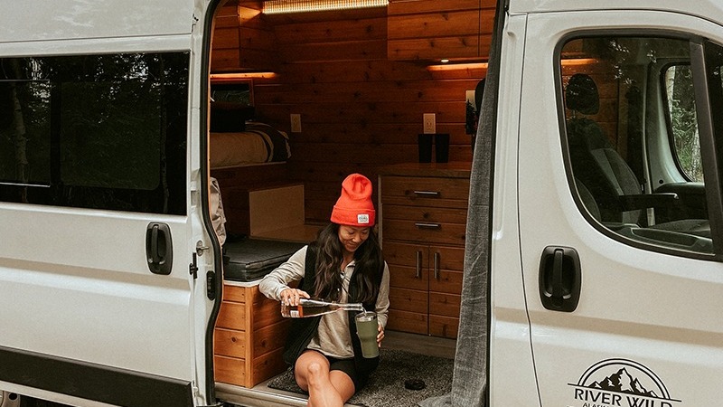 A person sitting in the doorway of a van converted into a cozy living space.