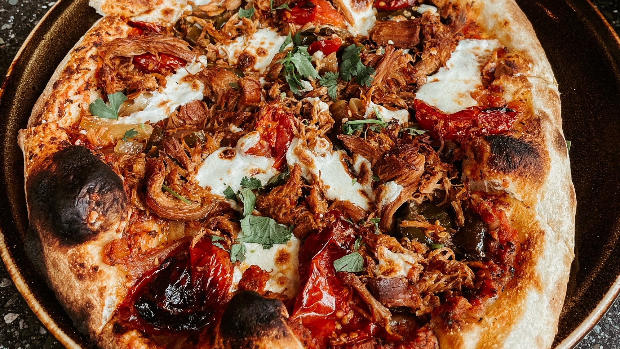 A freshly baked pizza with various toppings on a dark countertop.