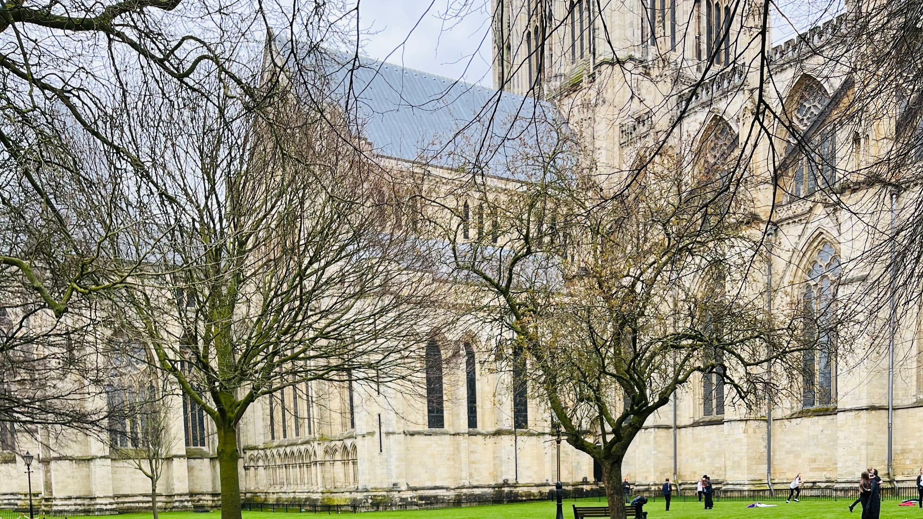 Exterior view of a Cathedral with some bare trees and people on the lawn.