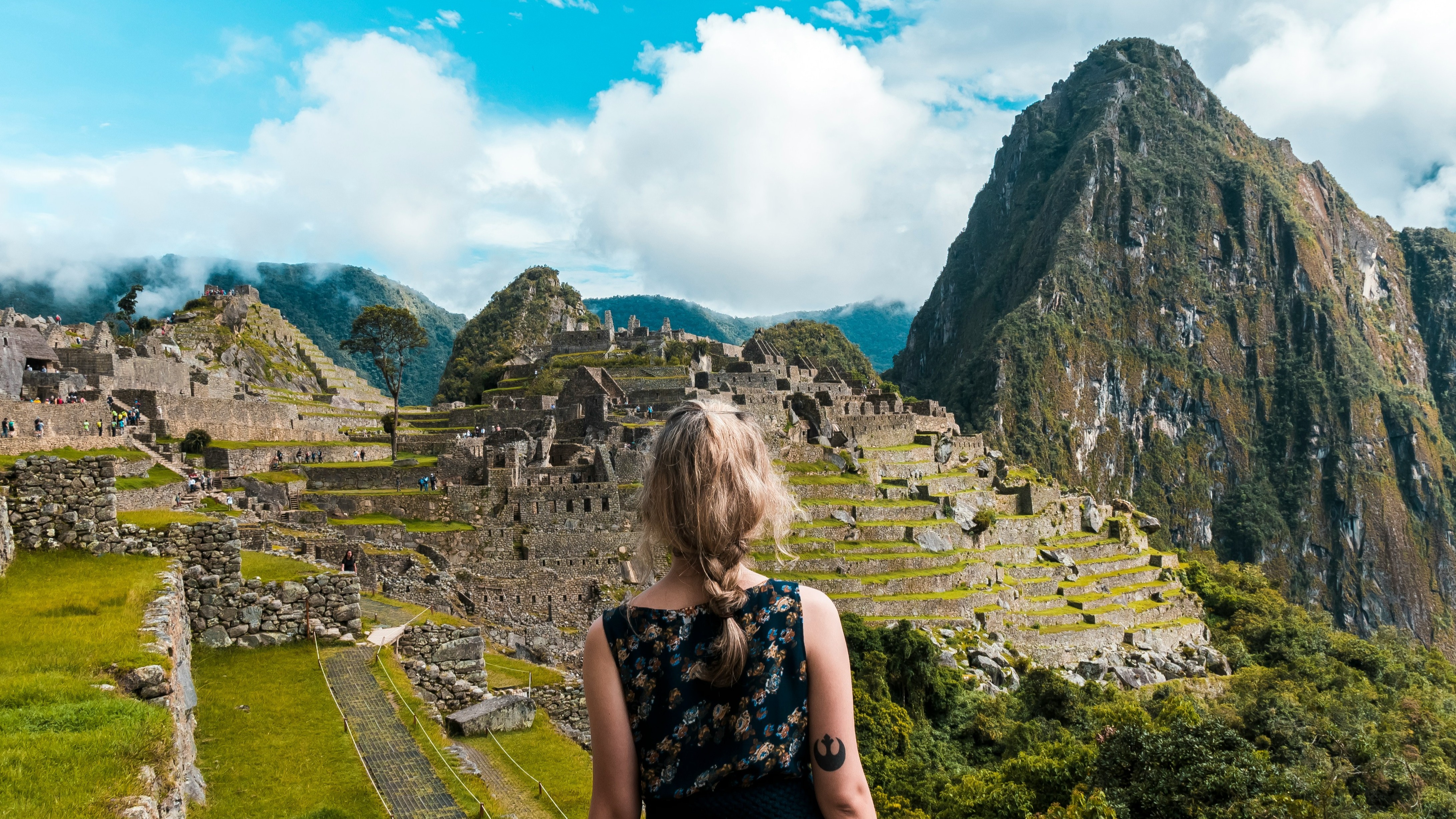 A person looks out over the ancient Incan city of Machu Picchu amidst a mountainous landscape under a partly cloudy sky.