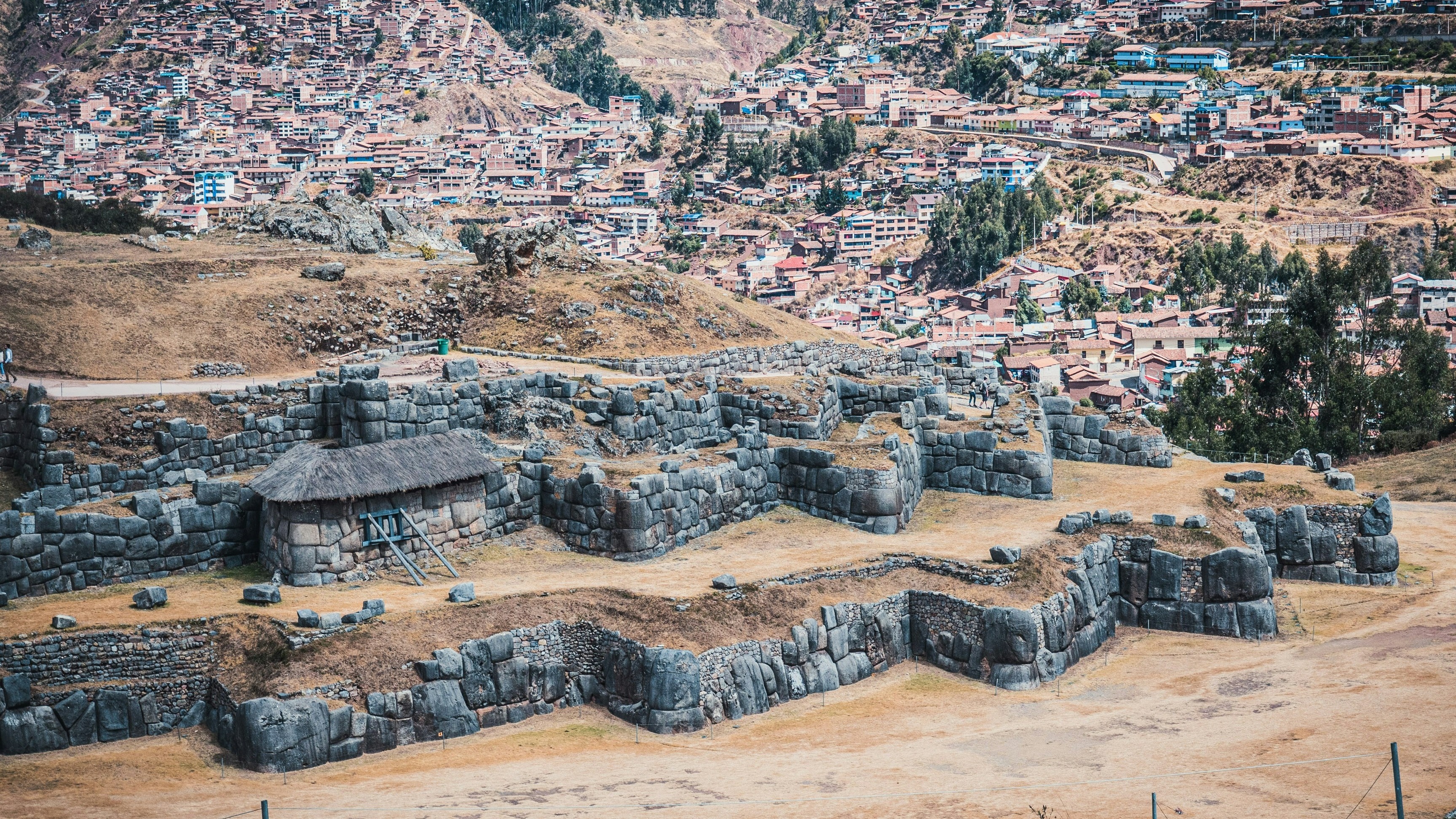 An archaeological site with large stone structures in the foreground and a densely built hillside city in the background.