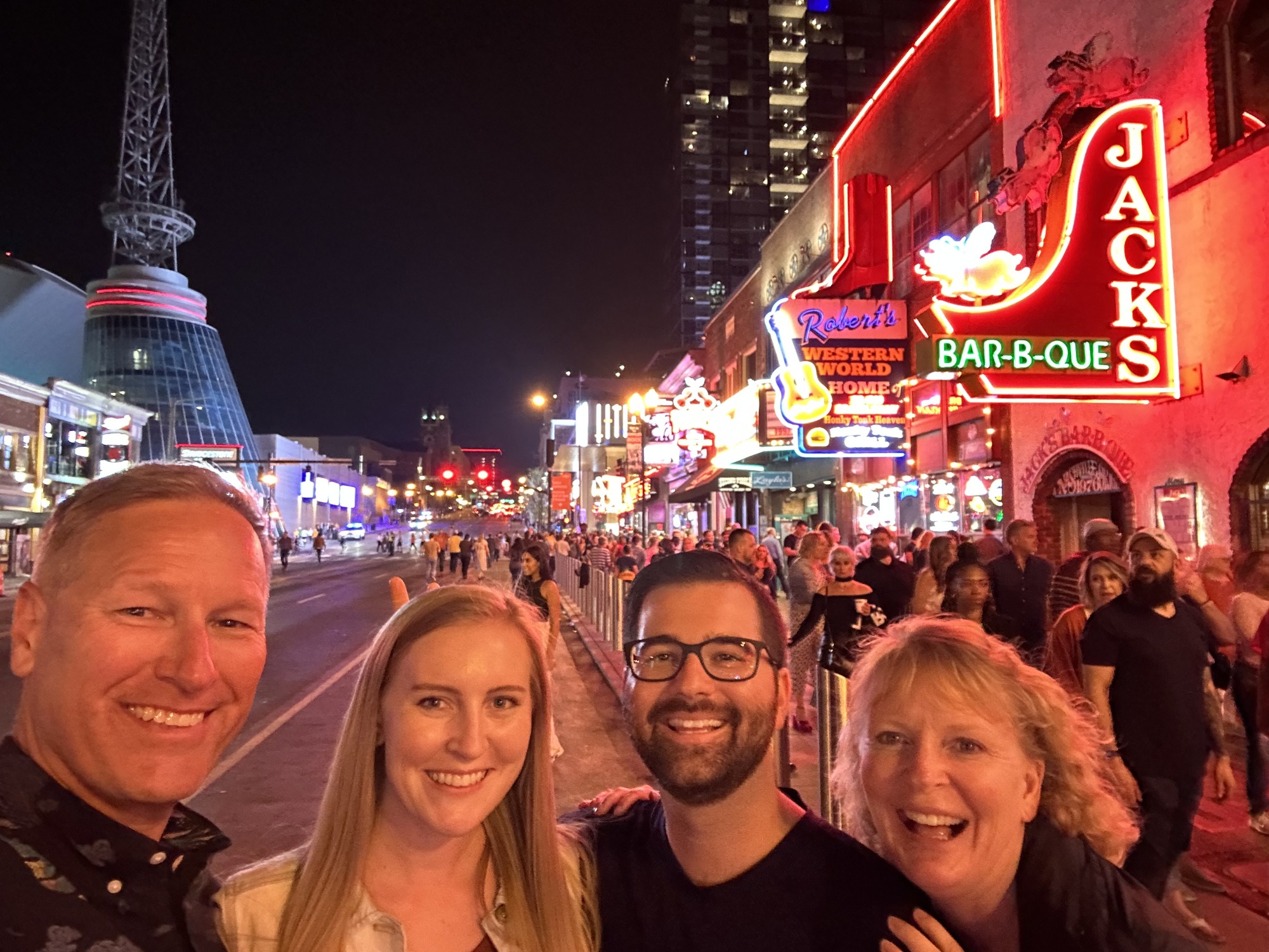 A group of people smiling for a selfie photograph in front of a busy city street at nighttime