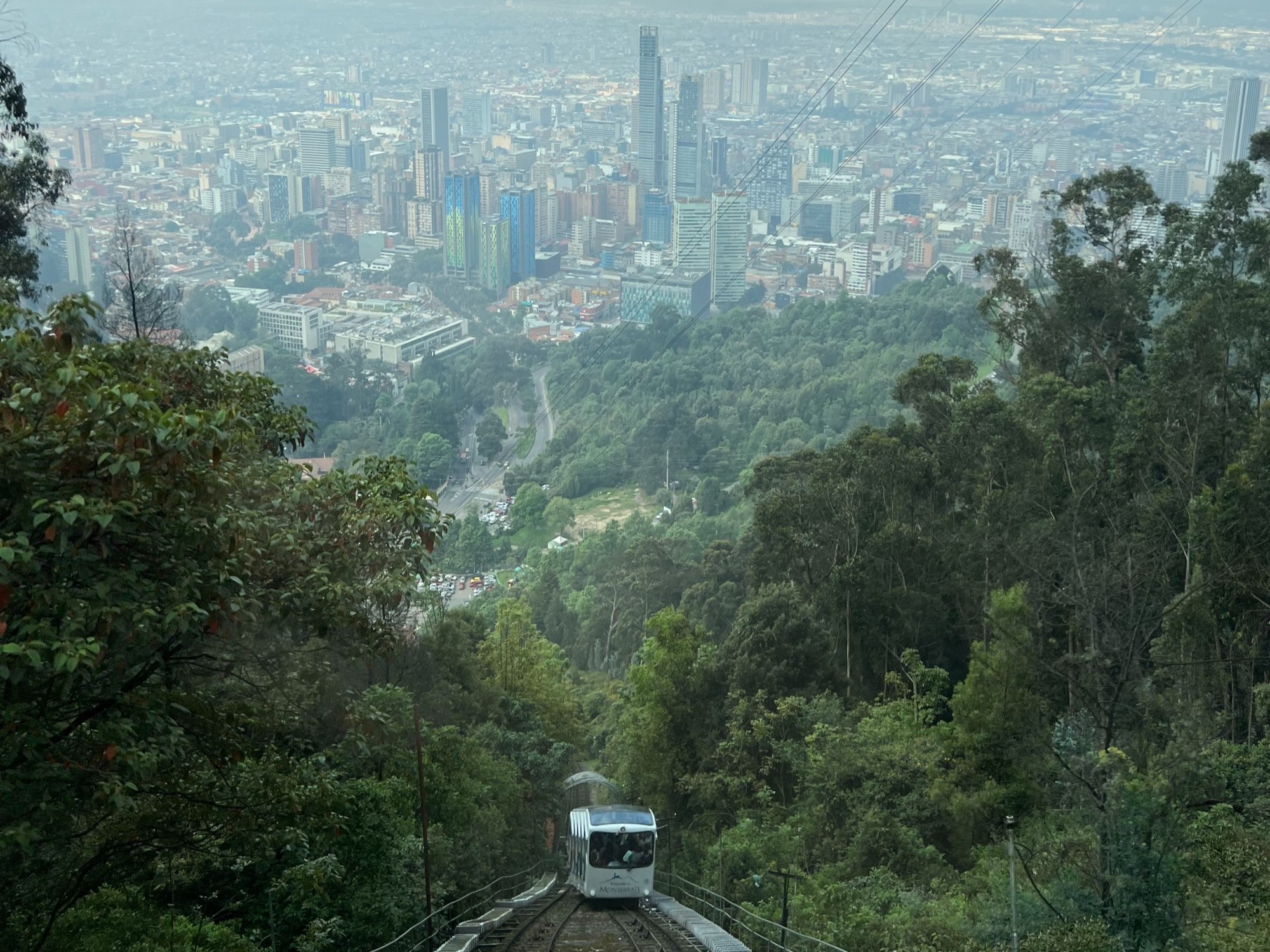 A cable car moving up a hill with a view of a large city in the distance
