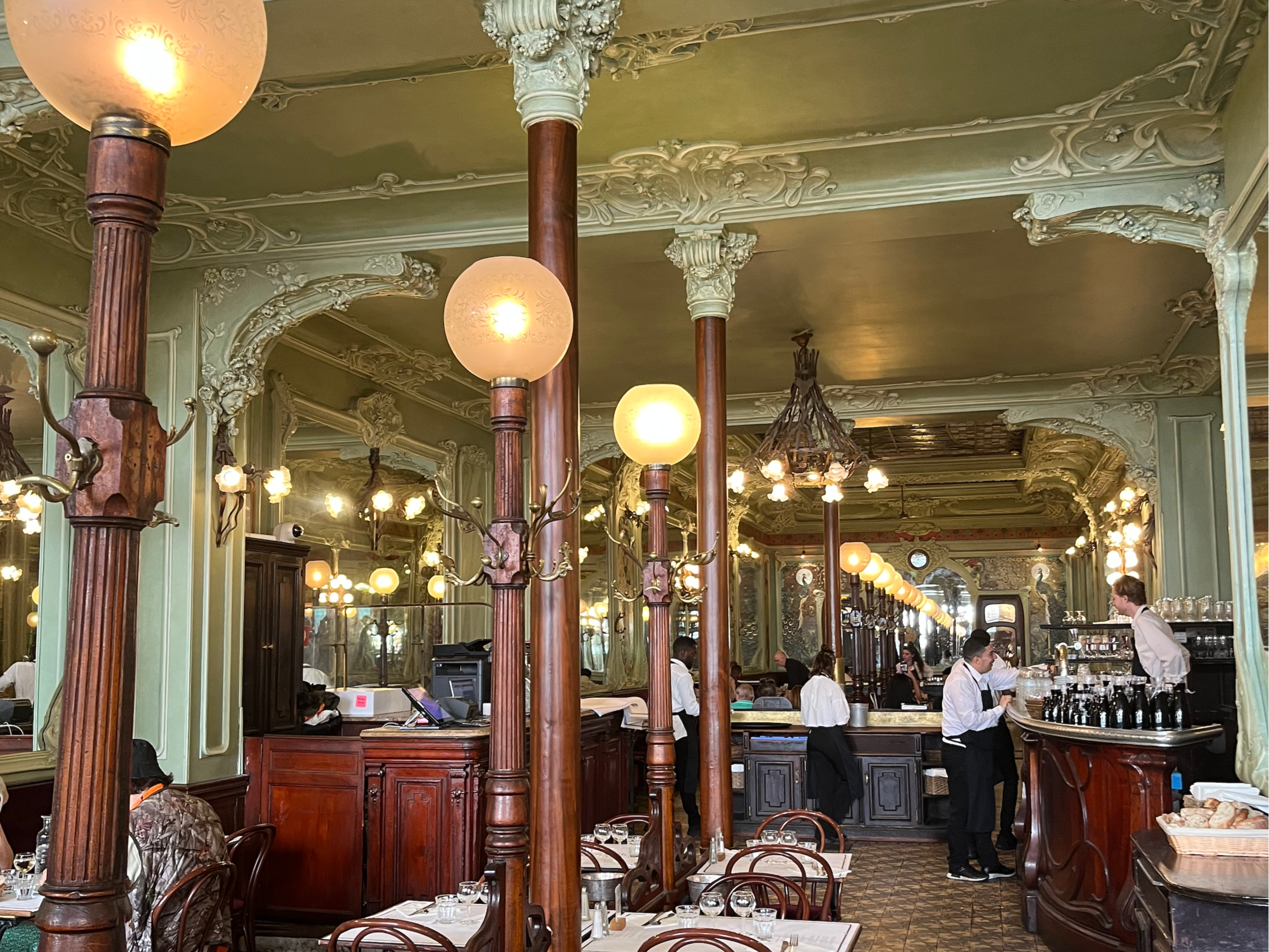 An ornate, vintage-style café interior with elaborate ceiling moldings and wooden furnishings.
