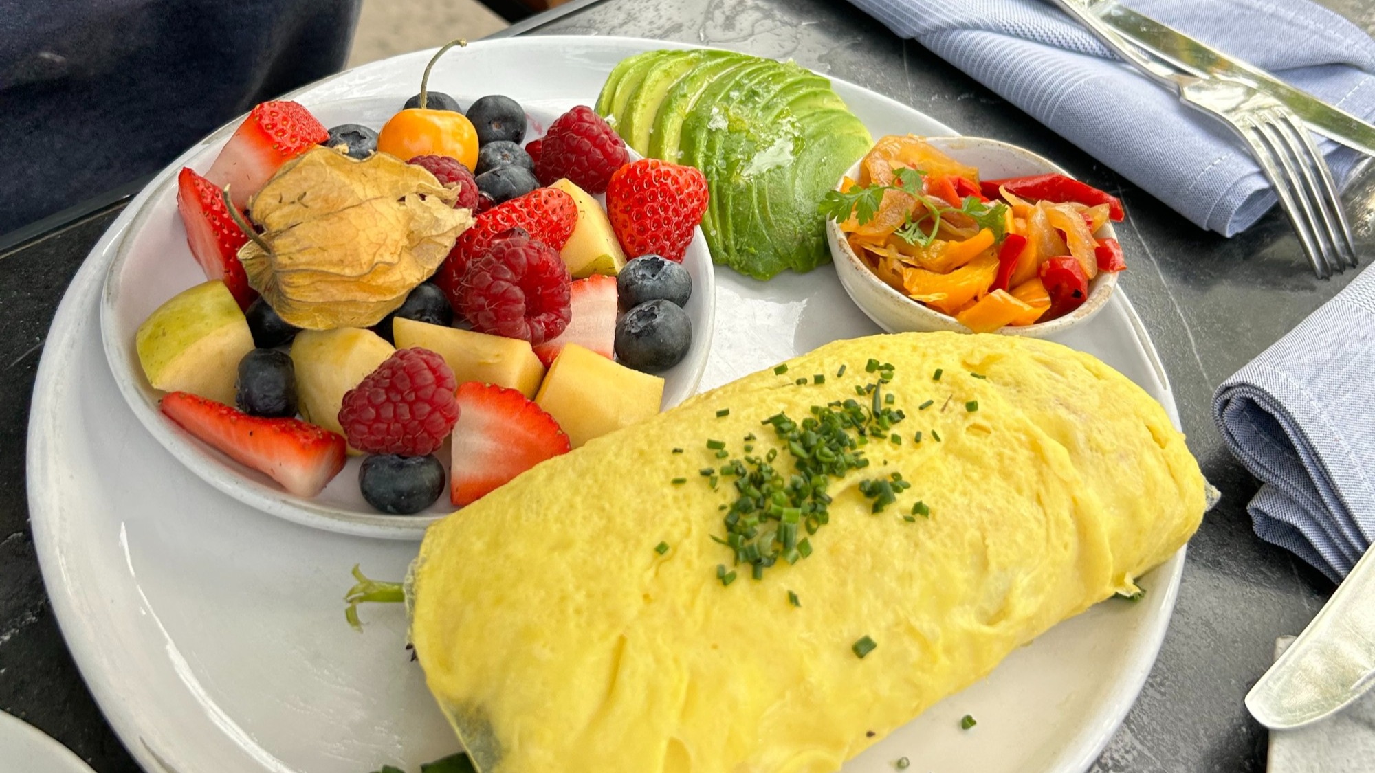 A plate of breakfast food including an omelette and a fruit cup.