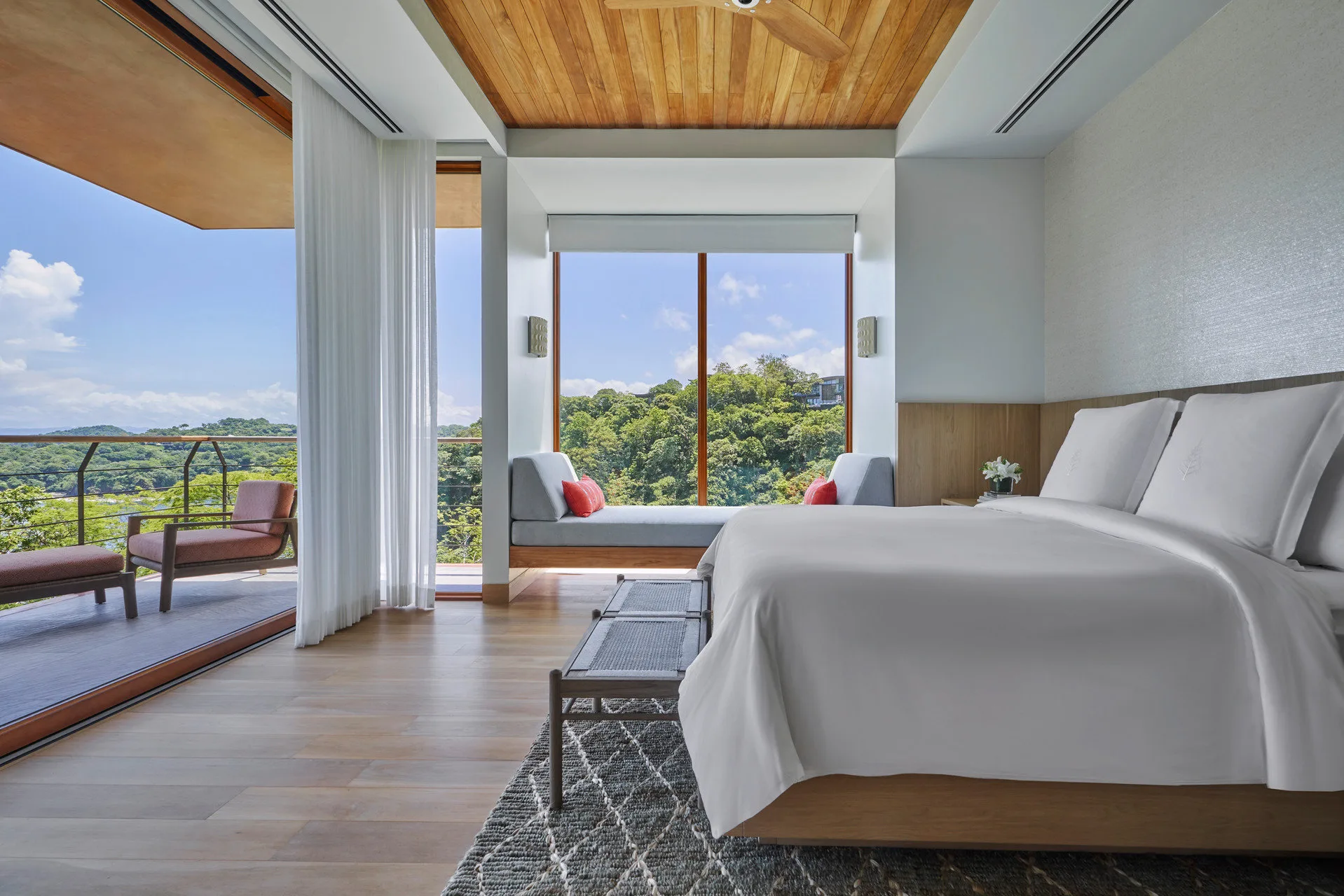 Massive suite with an oversized bed, loungers, a private balcony and floor-to-ceilings windows revealing a top-down view of the surrounding jungle