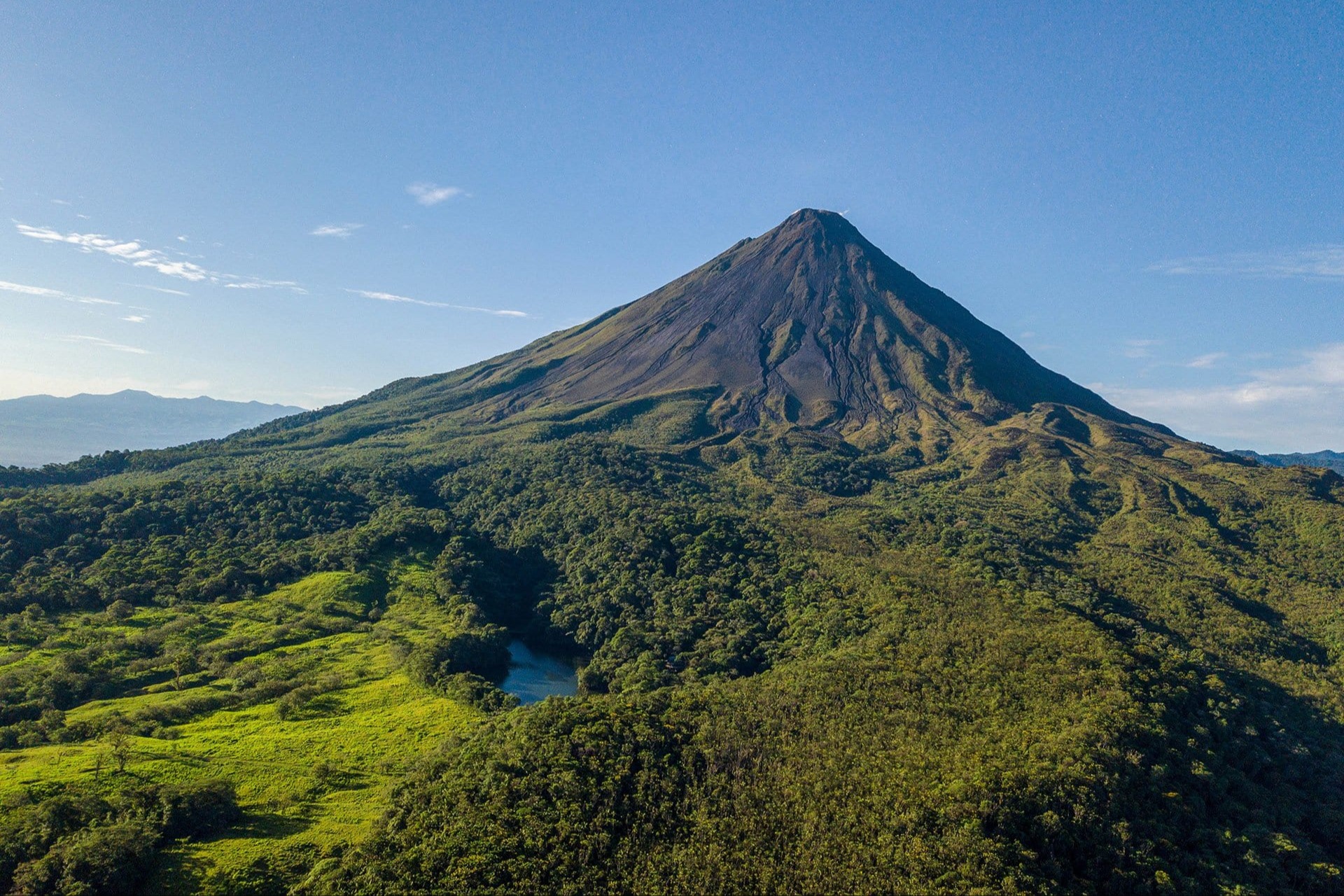 Aerial view of rainforest bisected by a jungle river leading up to Mount Arenal Volcano