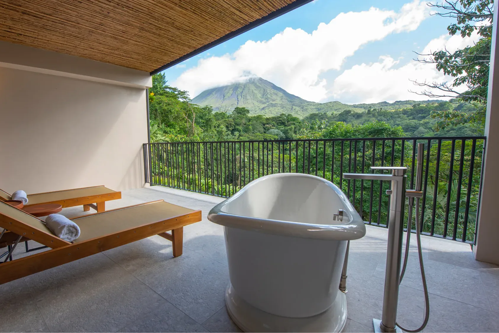 Twin loungers next to a deep soaking tub on a private balcony overlooking the Costa Rican jungle and Mount Arenal