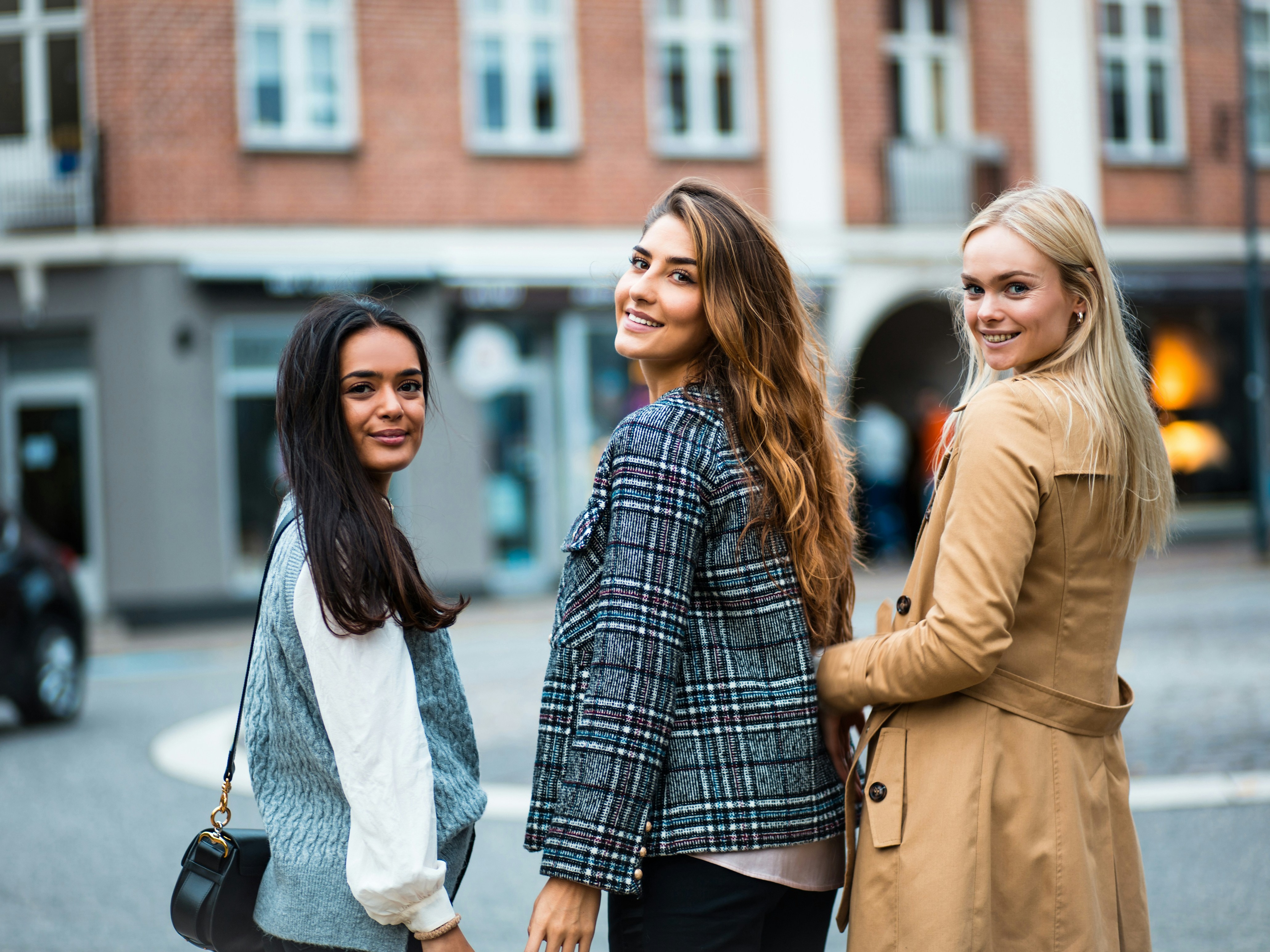 Three individuals are standing on the corner of a bustling street corner smiling.
