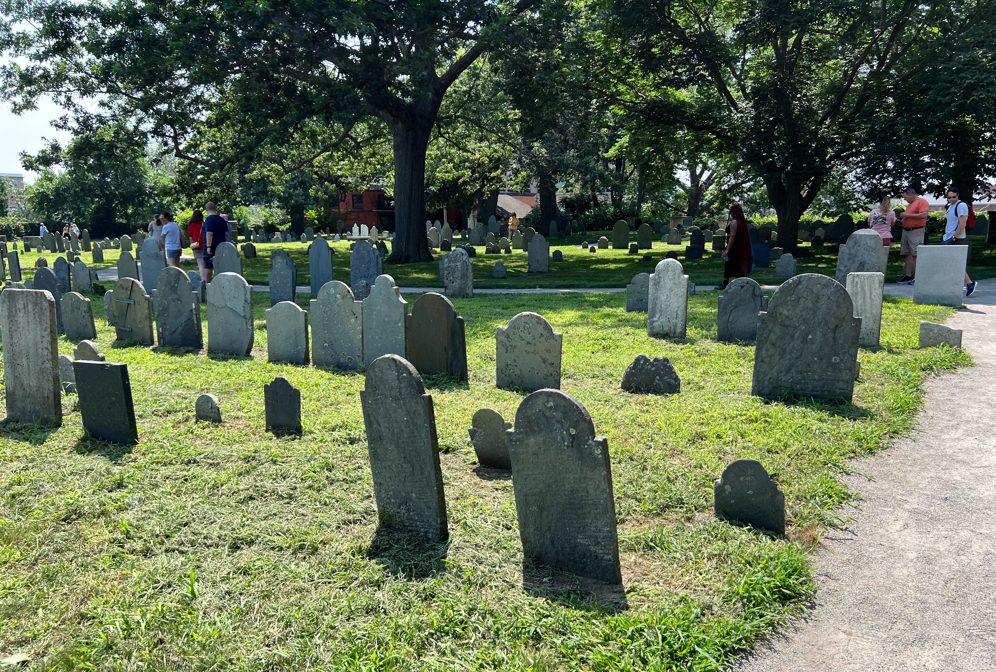 A cemetery with numerous headstones and people walking among lush greenery.