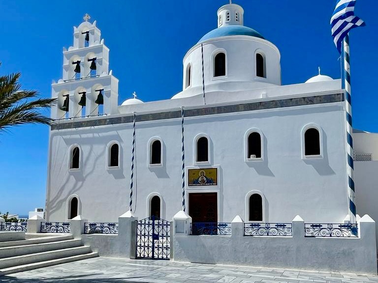 A white church with blue accents and multiple bell towers stands under a clear blue sky.