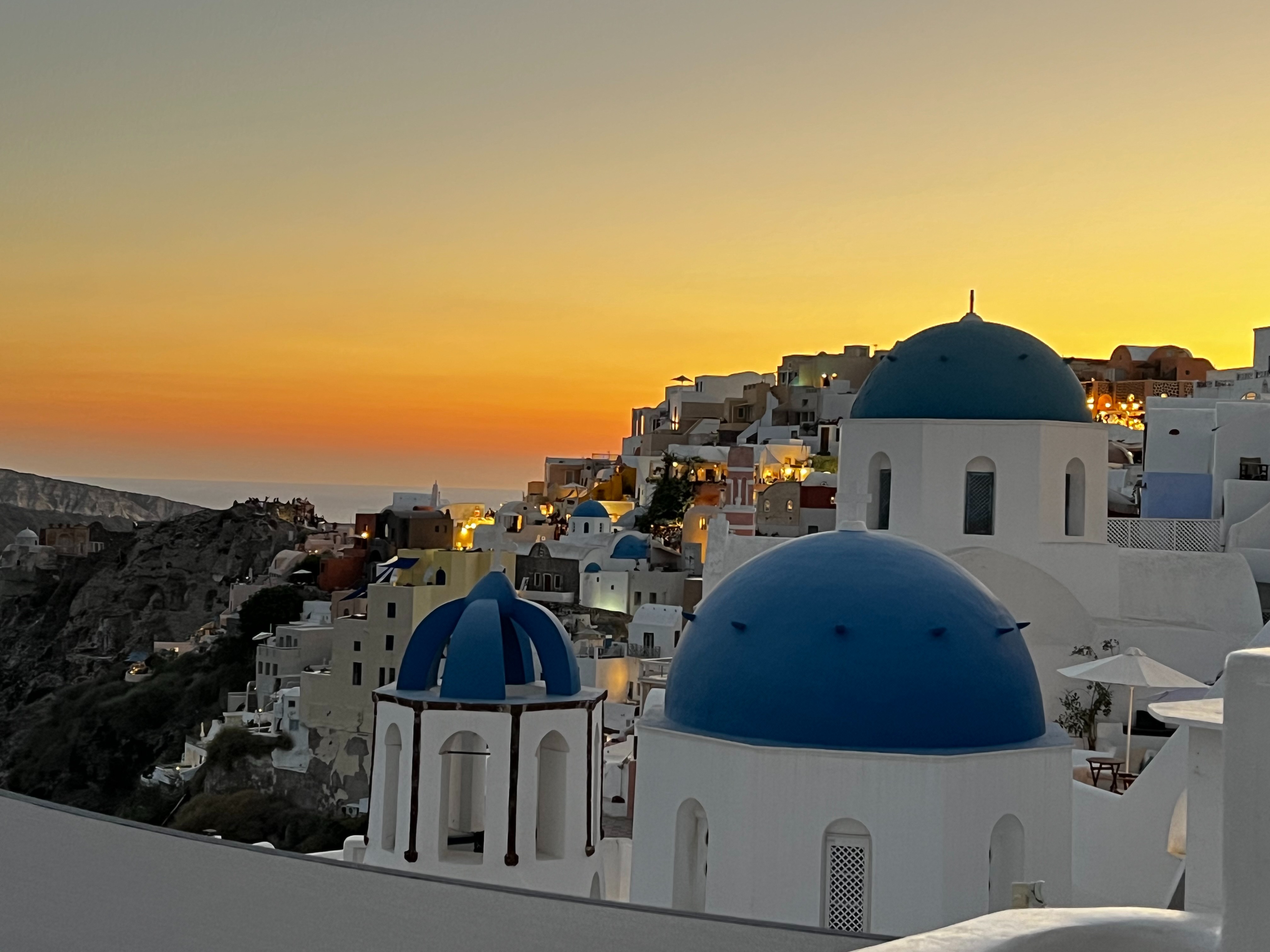 A sunset view of Santorini’s iconic blue-domed buildings against a vibrant sky.