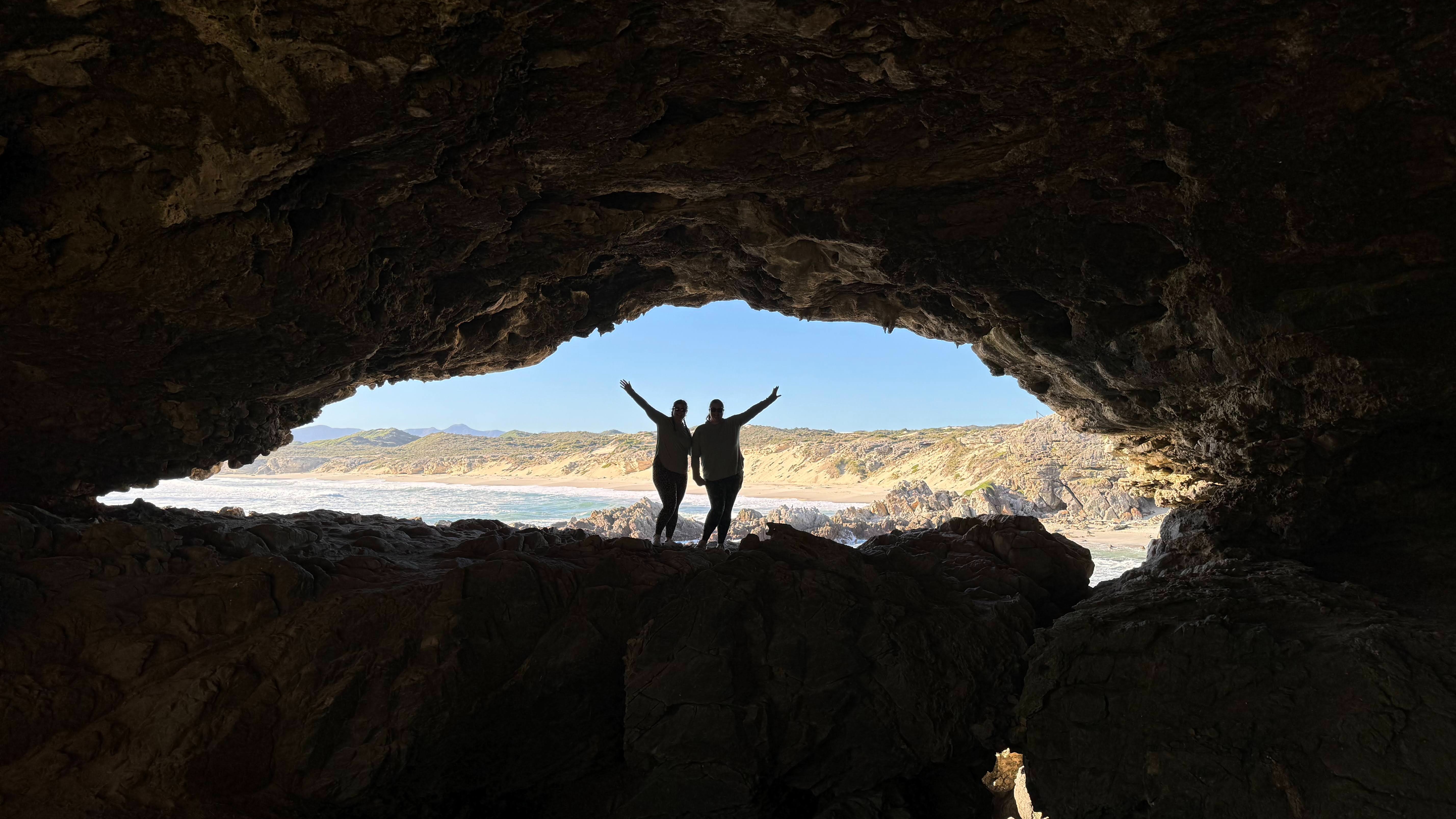 Two figures silhouetted in the entrance of a cave.
