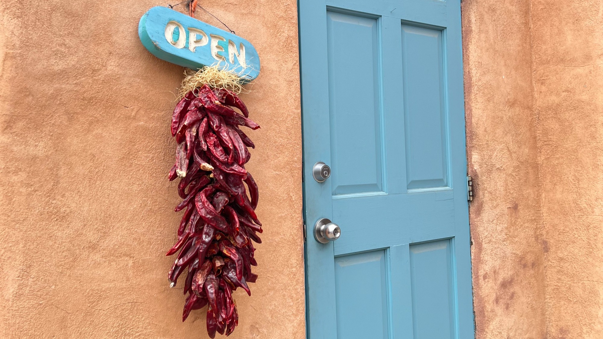 Chili peppers hanging next to a blue door on an adobe building.
