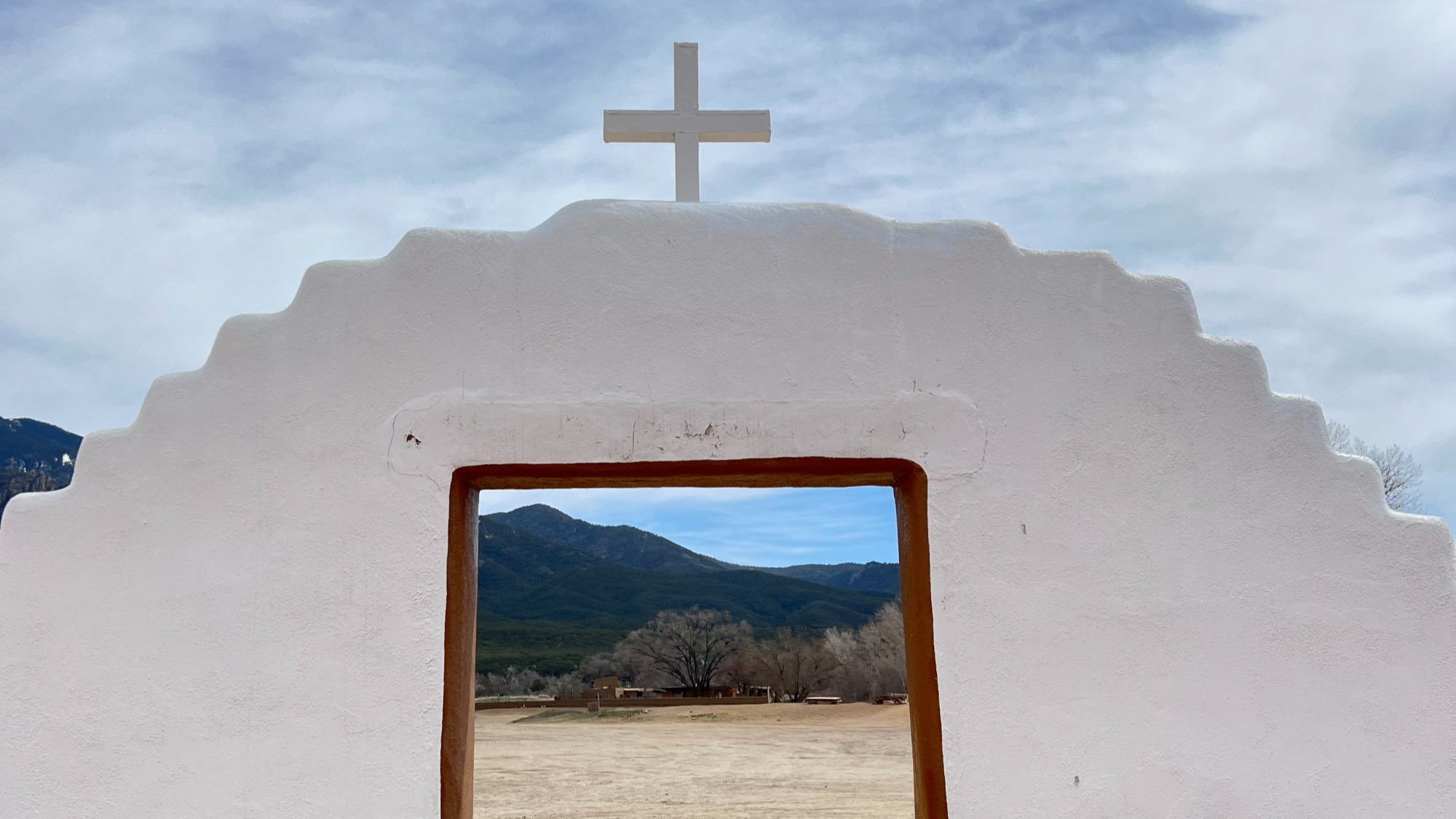 A white adobe door frame that leads out of a courtyard into the desert.