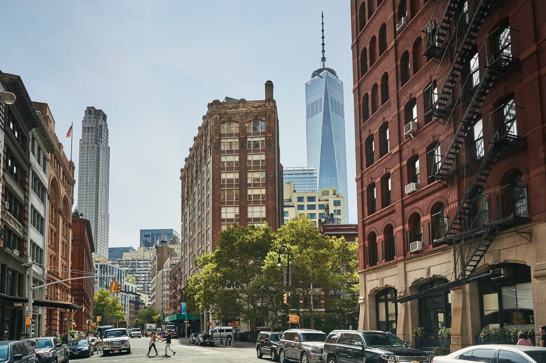 An ordinary street in TriBeCa with a few locals walking by and One World Trade Center standing prominently in the distance