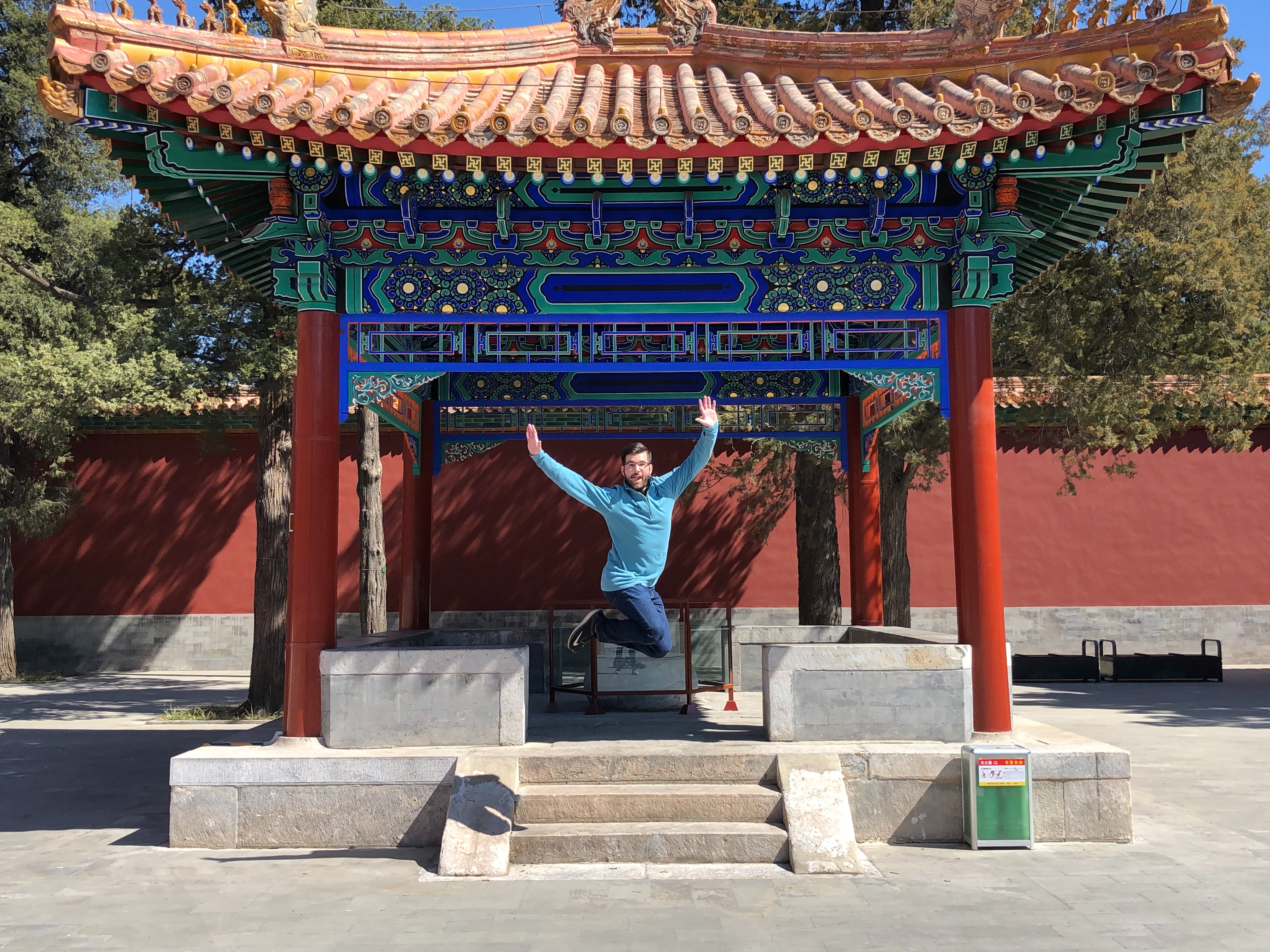 A person jumping and posing for a photograph underneath a traditional Chinese pavilion