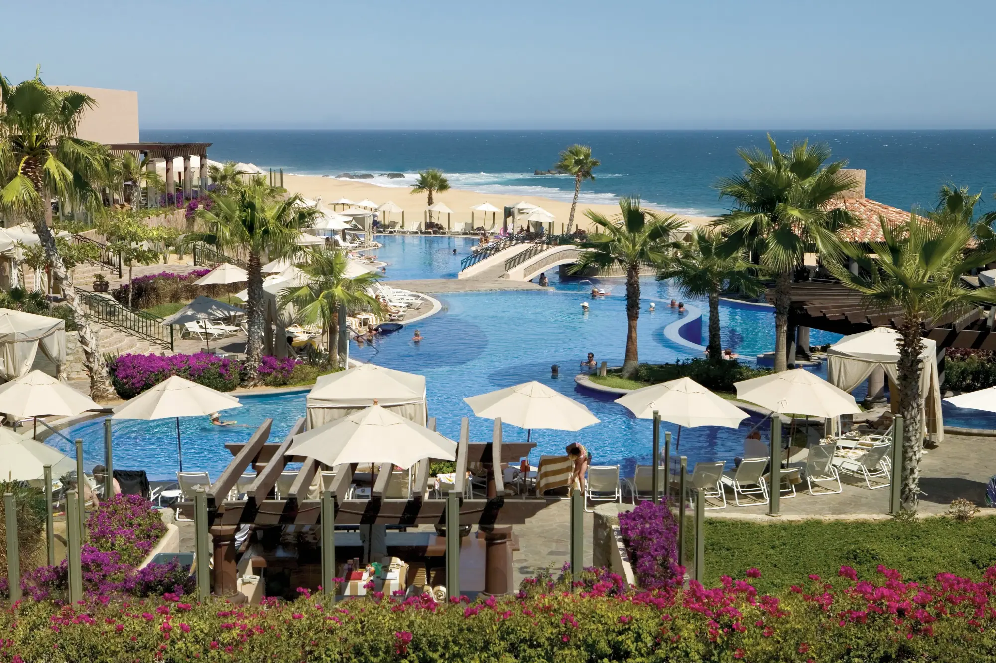 Large umbrellas, awnings and palm trees dot a massive pool complex that eventually leads to the shoreline of Cabo San Lucas