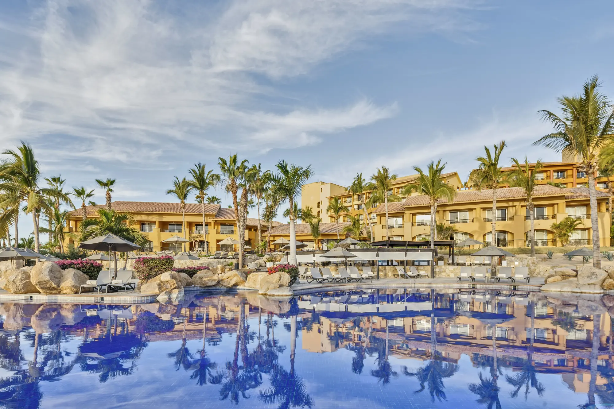 Palm trees and the structure of Grand Fiesta Americana Los Cabos reflect off a huge pool