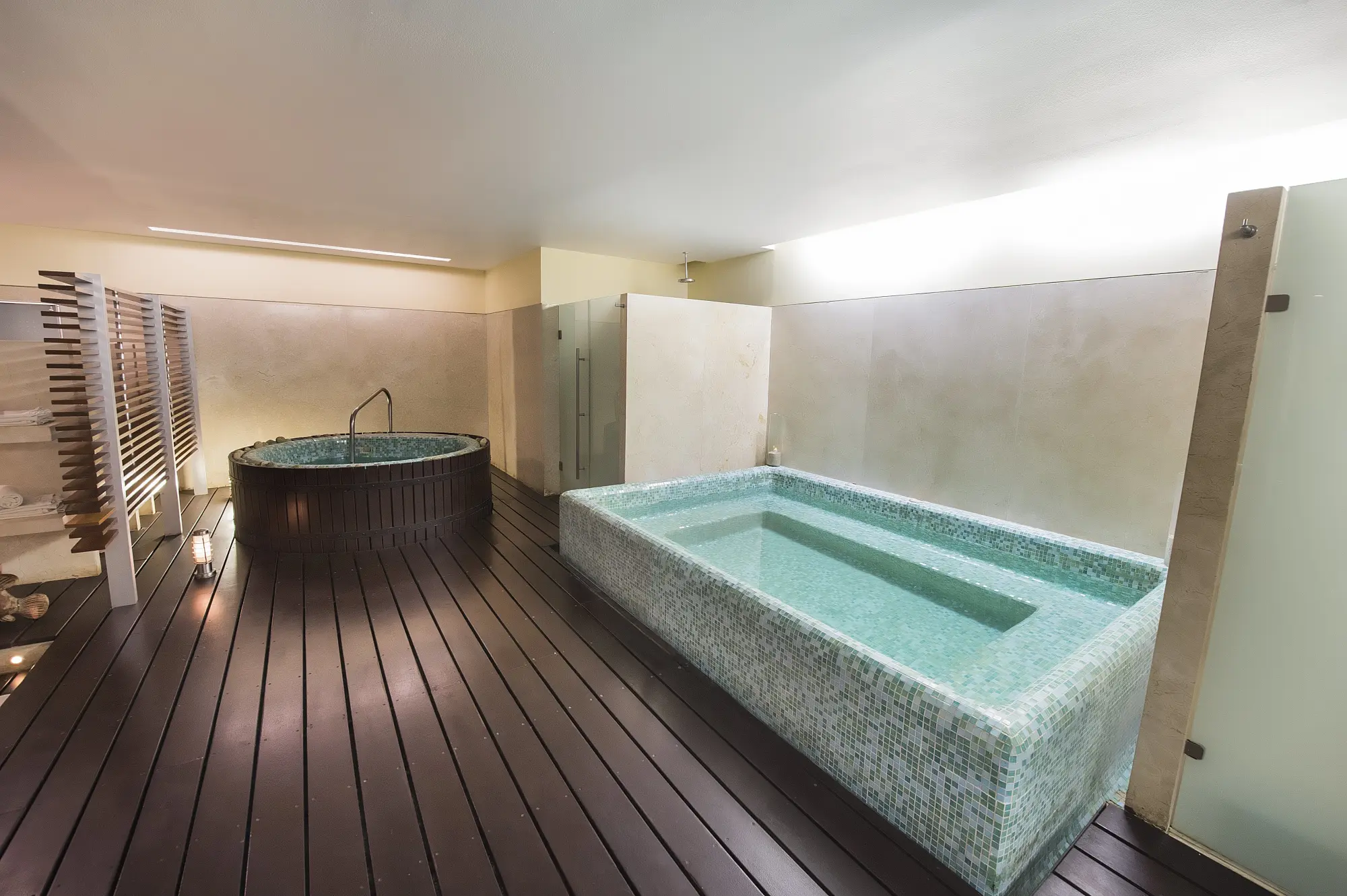 Dark hardwood floors surrounded a deep marble soaking tub next to a hardwood-clad hot tub in a sauna-like room