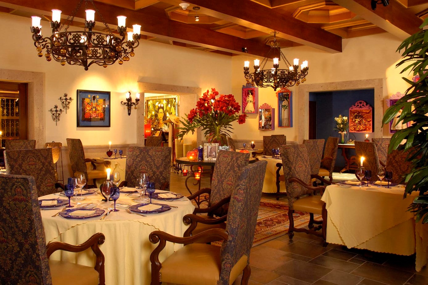 Elegant table settings beneath chandeliers and warm lighting. Mexican art dots the walls