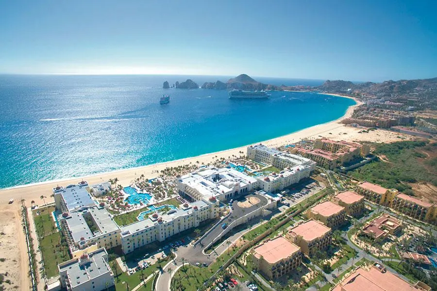 Aerial view of Hotel Riu Palace Cabo with the massive, whitewashed resort sitting on the beach and the sapphire bay just past the shoreline