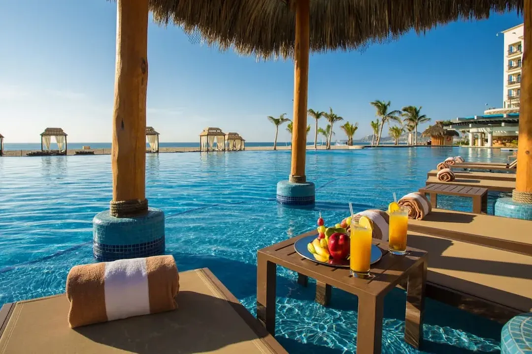 Loungers and tables sit directly in a sapphire-blue pool with ocean views