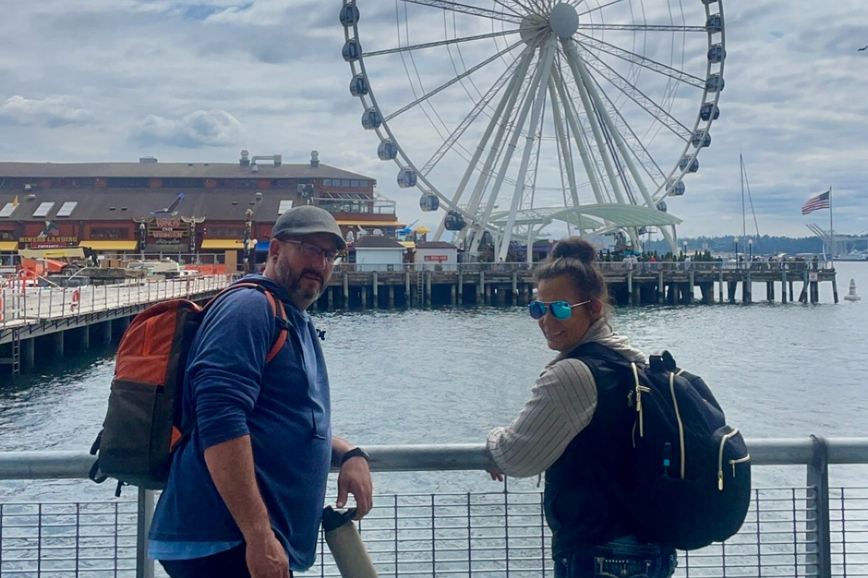 The advisor and a man posing on a pier over the water with a ferris wheel in the background at Miners Landing, Seattle.