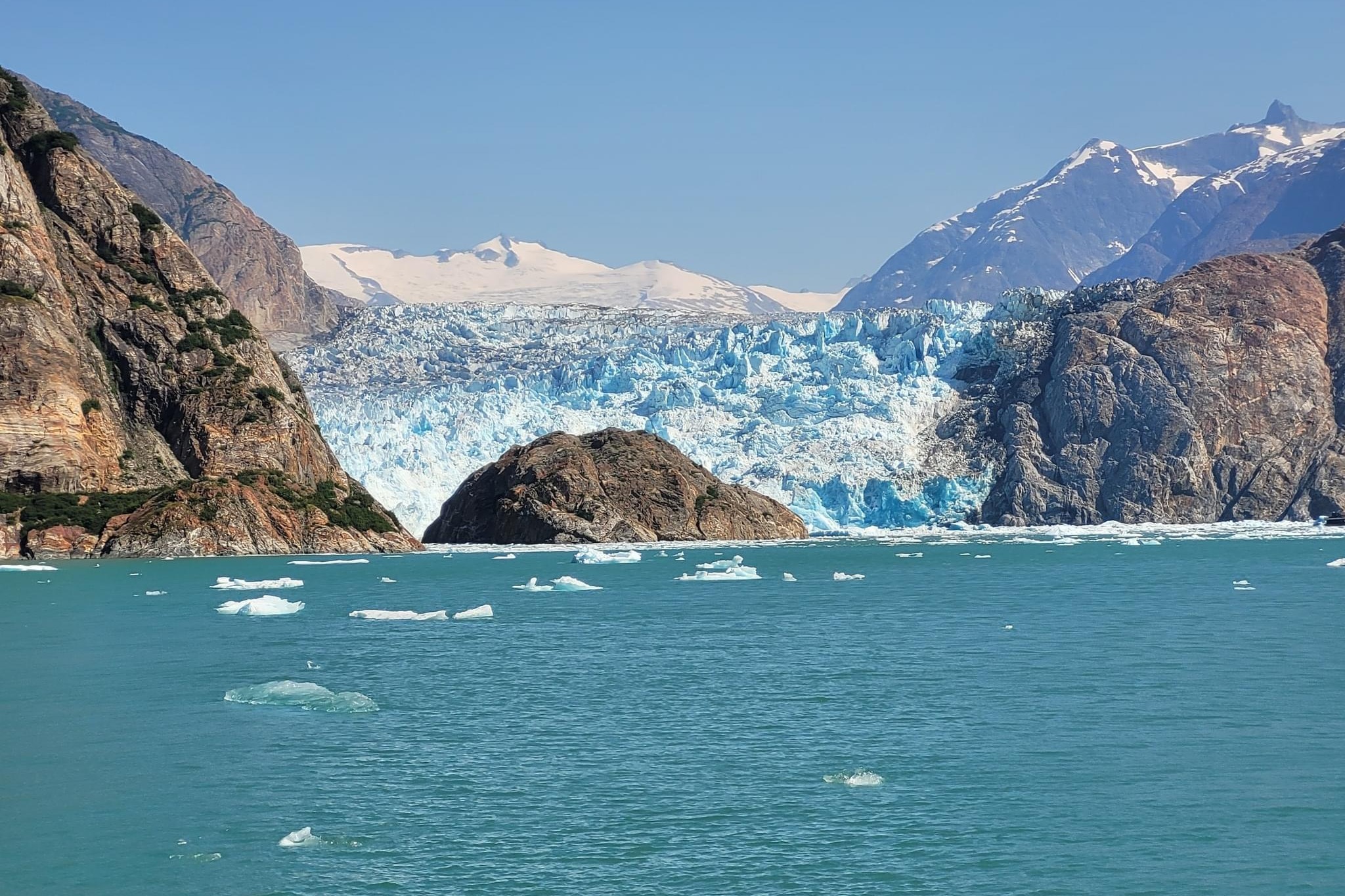 A view across the ocean of the Tracy Arm Fjord a glacier between two large mountains, during the day.