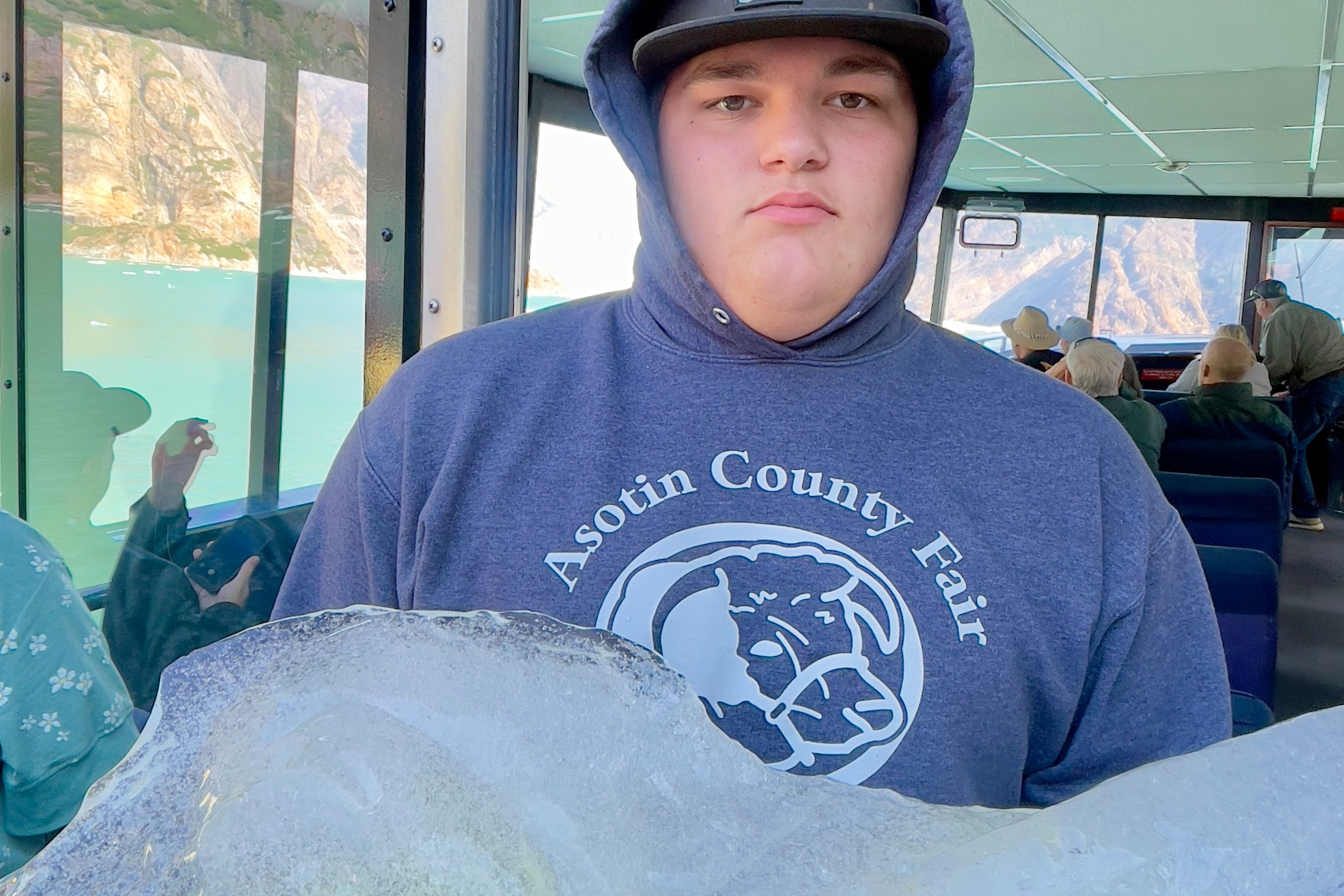 A boy holding a large piece of ice onboard a ship with mountains in the background.