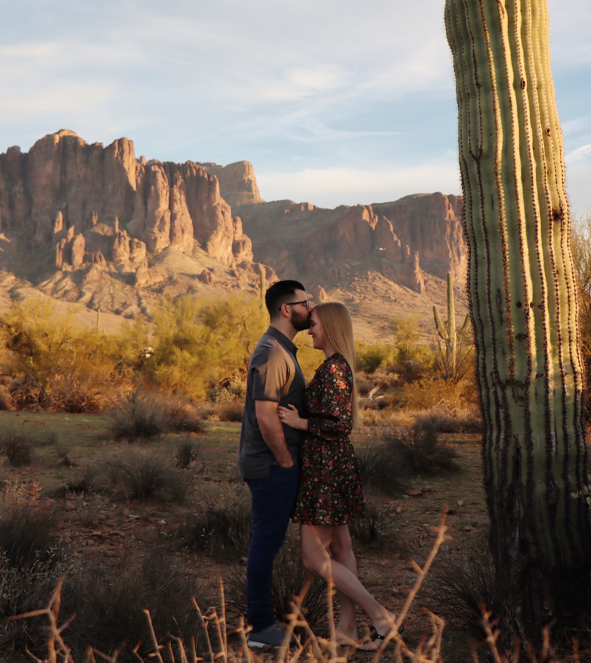A couple in the desert next to a cactus in the afternoon.