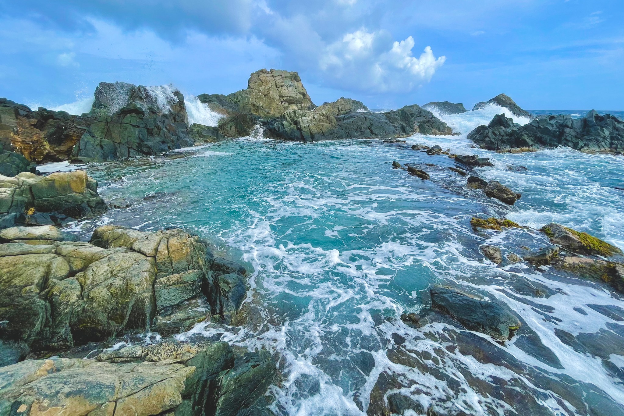 A natural pool formed in a body of water surrounded by large rocks during the daytime