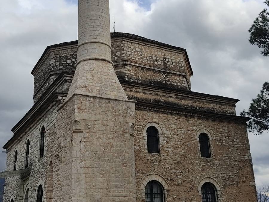 A historic stone building with a tall minaret stands majestically against a cloudy sky.