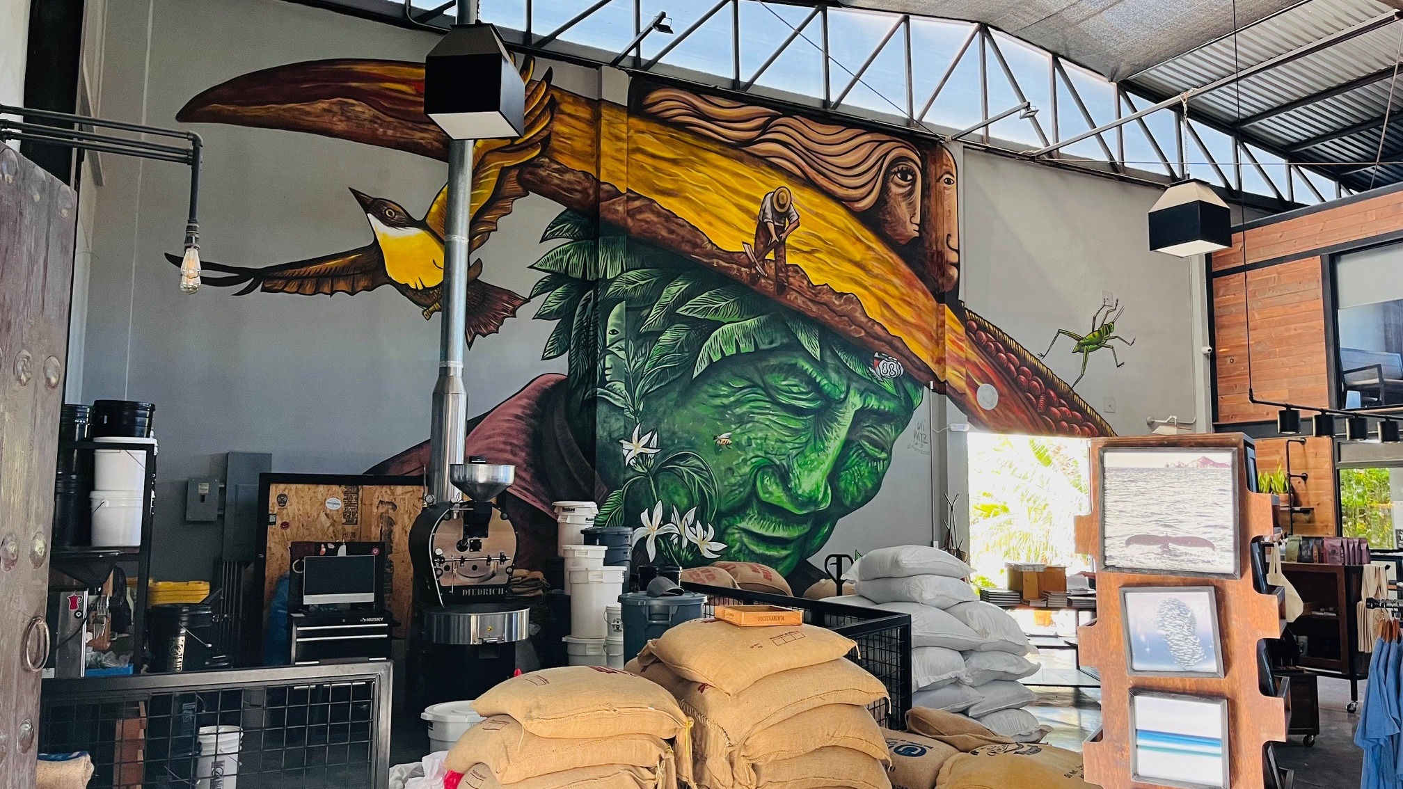 A large, colorful mural of a bird and a man in a hat adorns the wall of an indoor space filled with sacks and various items.
