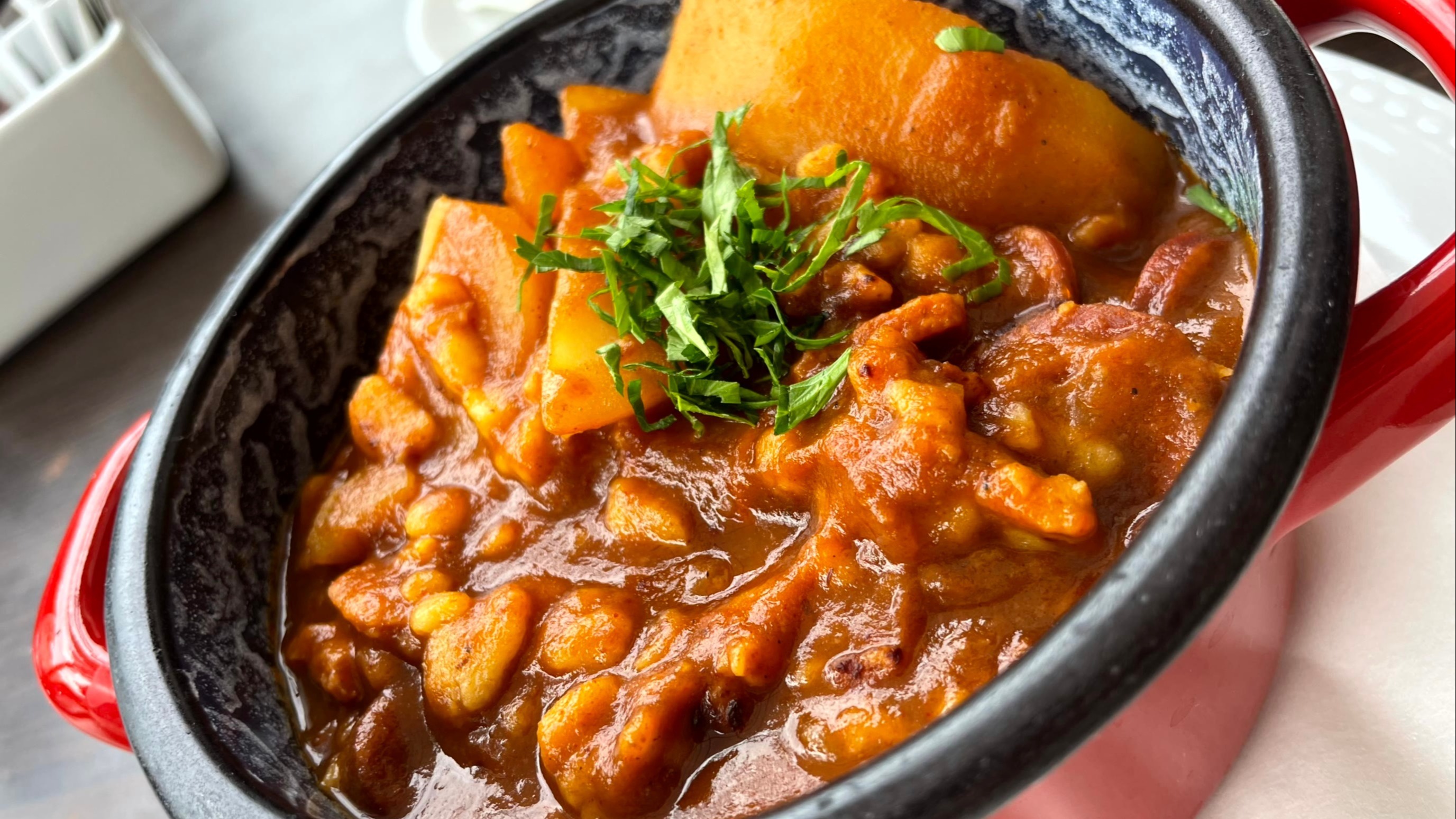 A close-up of a hearty stew with chunks of meat and vegetables garnished with fresh herbs.