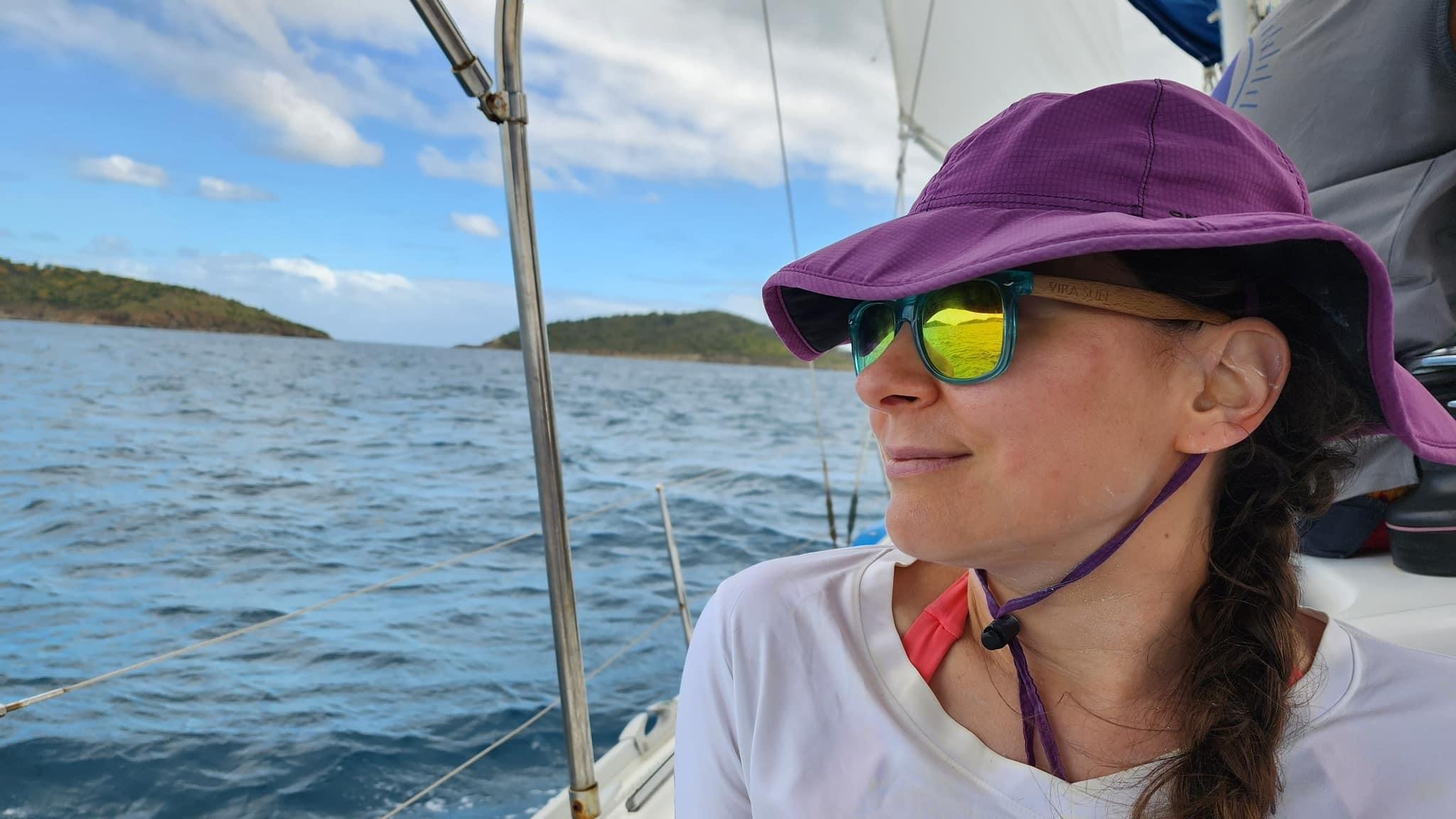 A person in a purple sun hat and mirrored sunglasses enjoys a peaceful sail with serene ocean views.