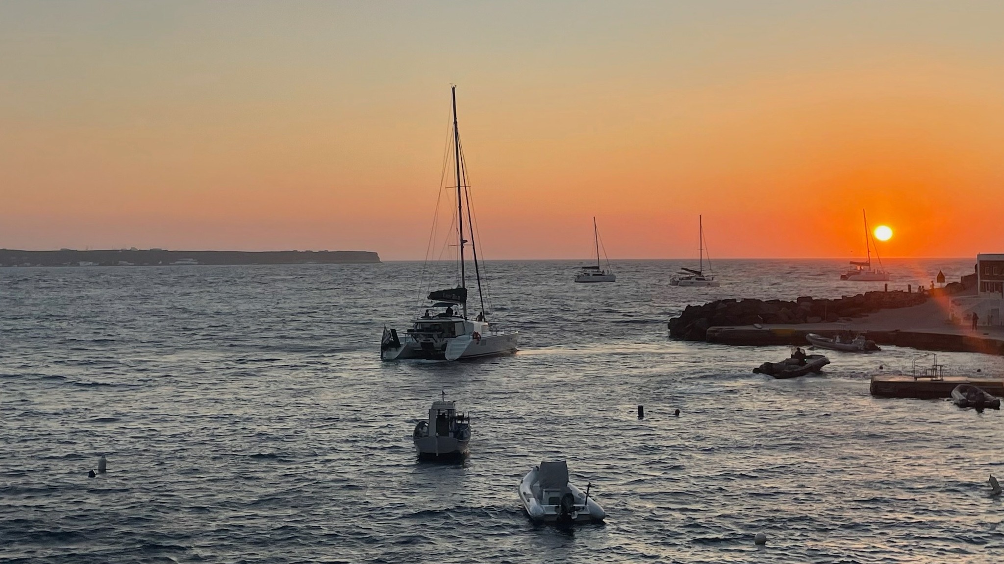 A serene sunset over a tranquil body of water with boats and a picturesque coastline.